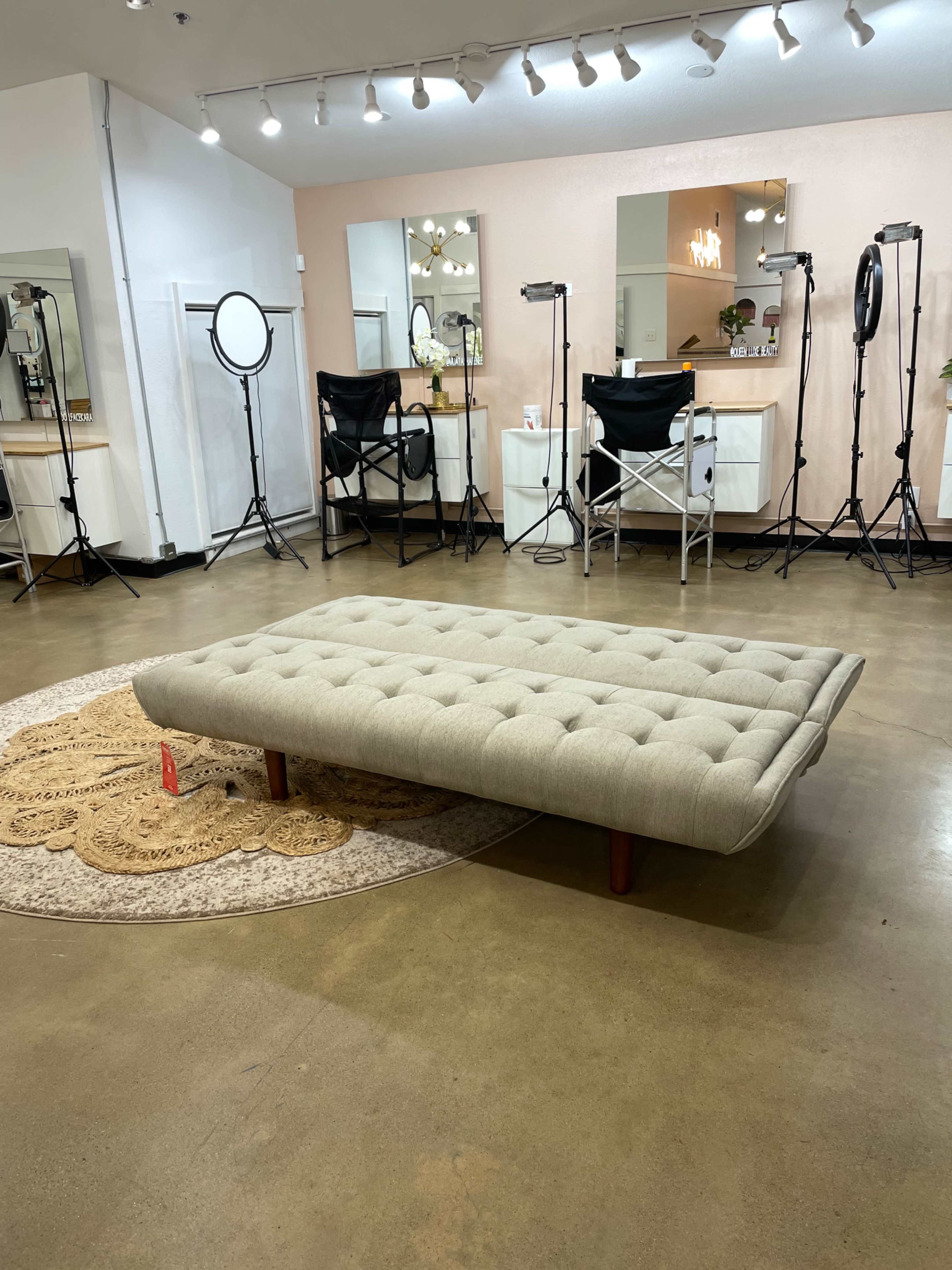 A spacious room with a light-colored floor, a large tufted sofa in the center, and several mirrors and lighting equipment arranged around the walls.