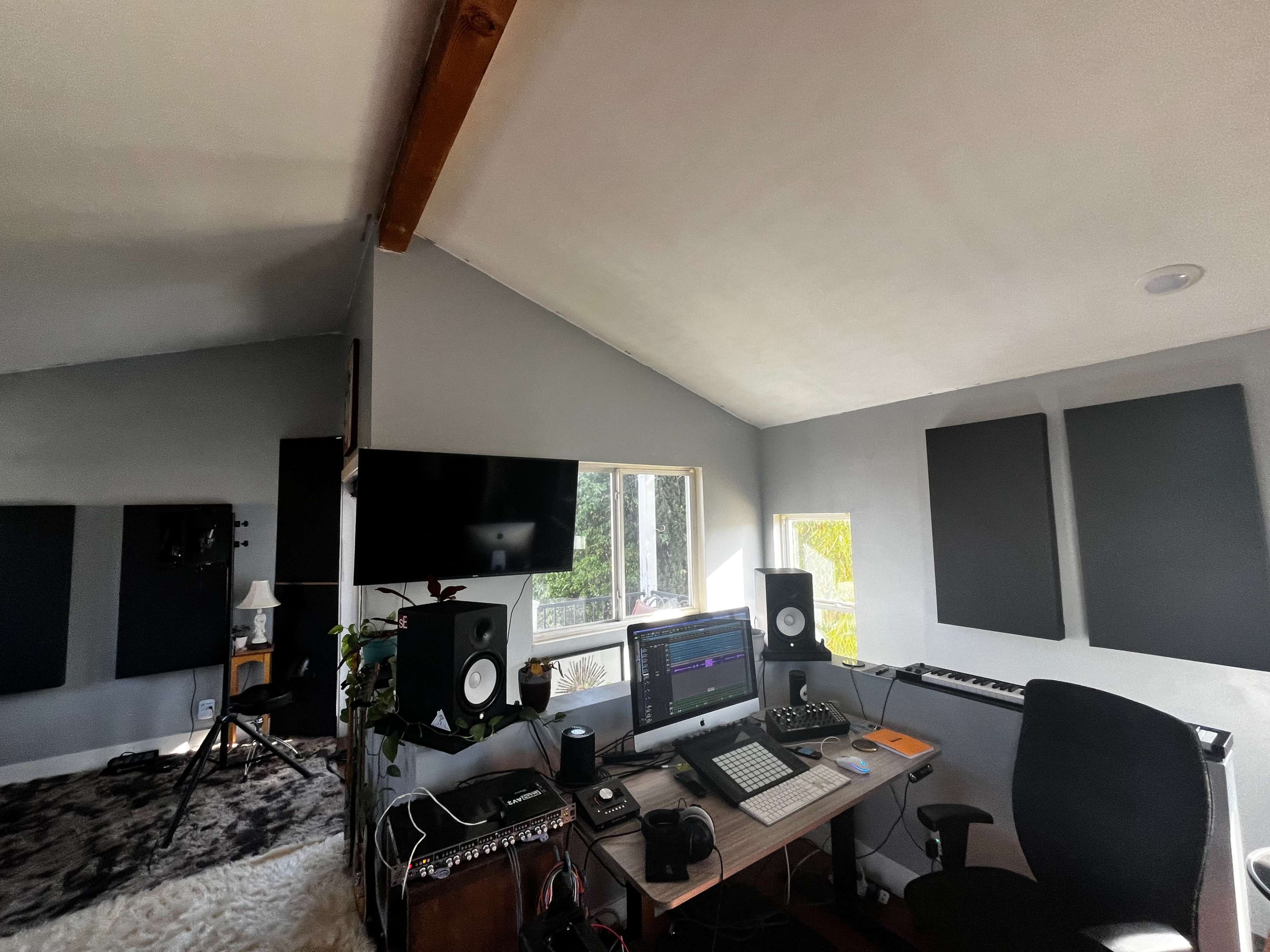 The image shows a music production studio with a computer setup, speakers, and soundproofing panels on the walls.