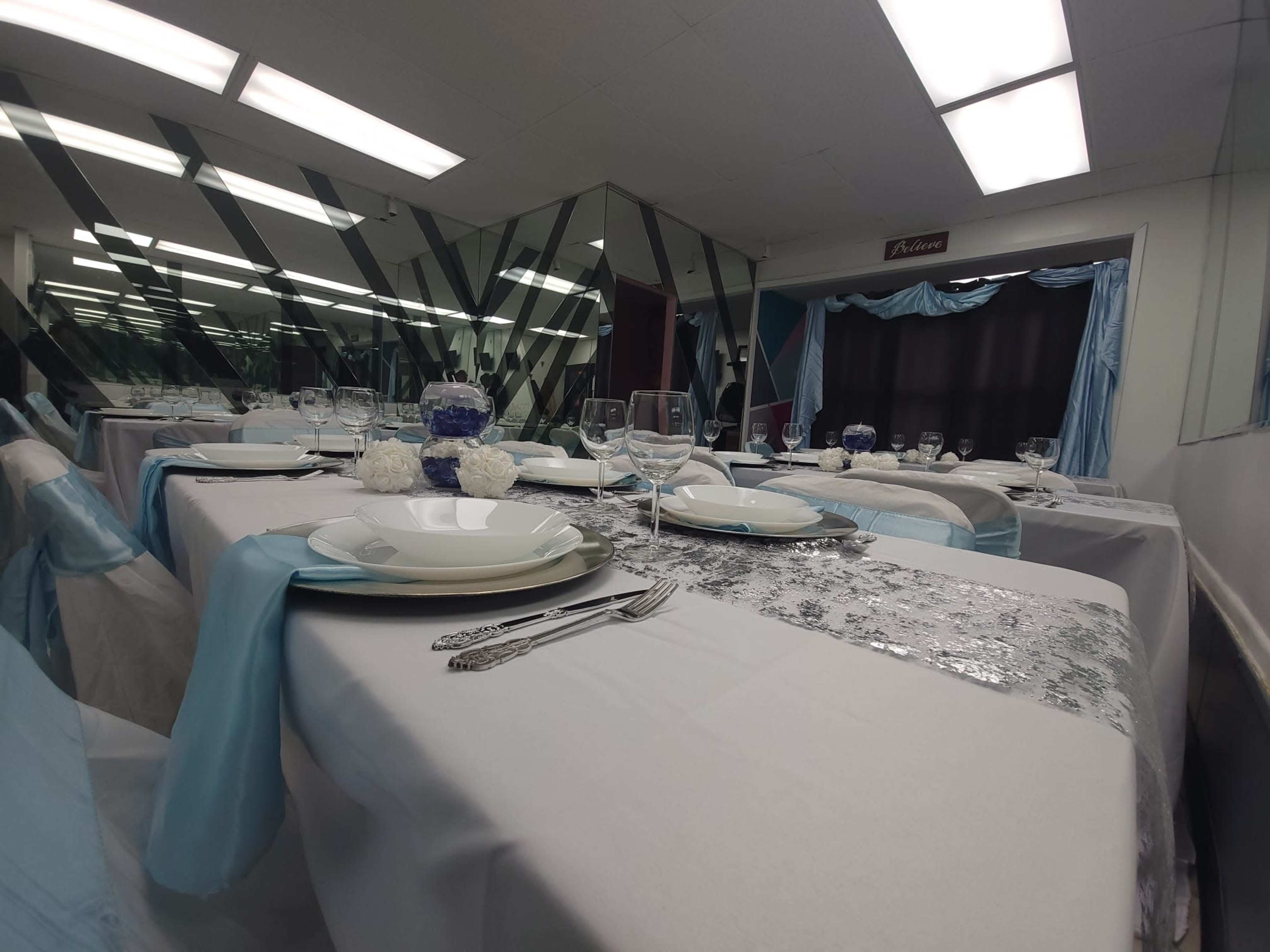 A banquet hall set for a formal event, featuring tables covered with white tablecloths and decorated with blue accents, plates, glasses, and centerpieces.