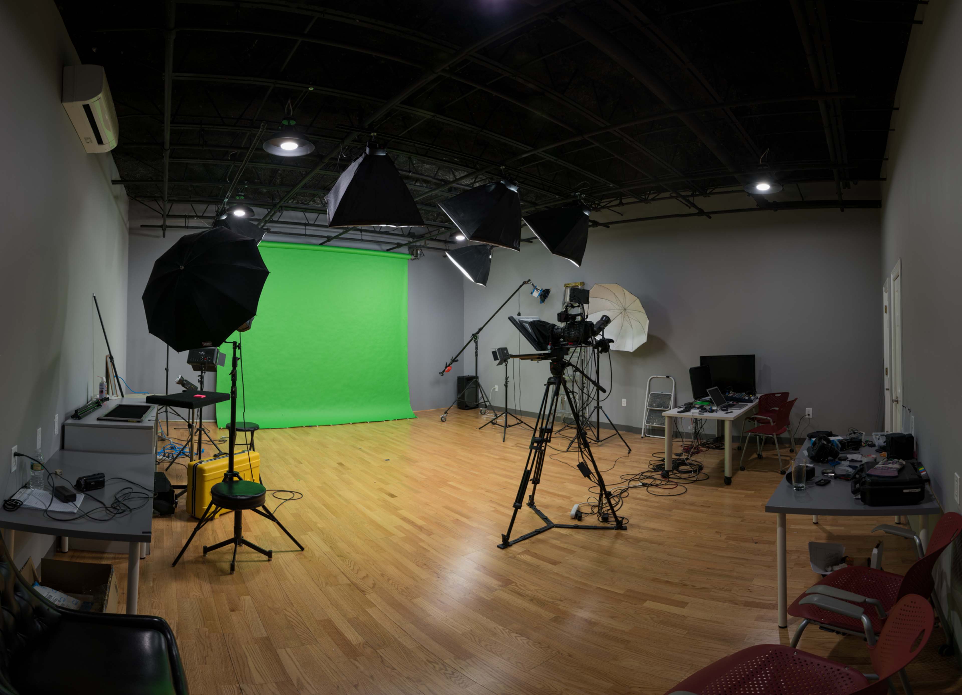 A photography studio equipped with a green screen, lighting equipment, and a camera setup on a wooden floor.