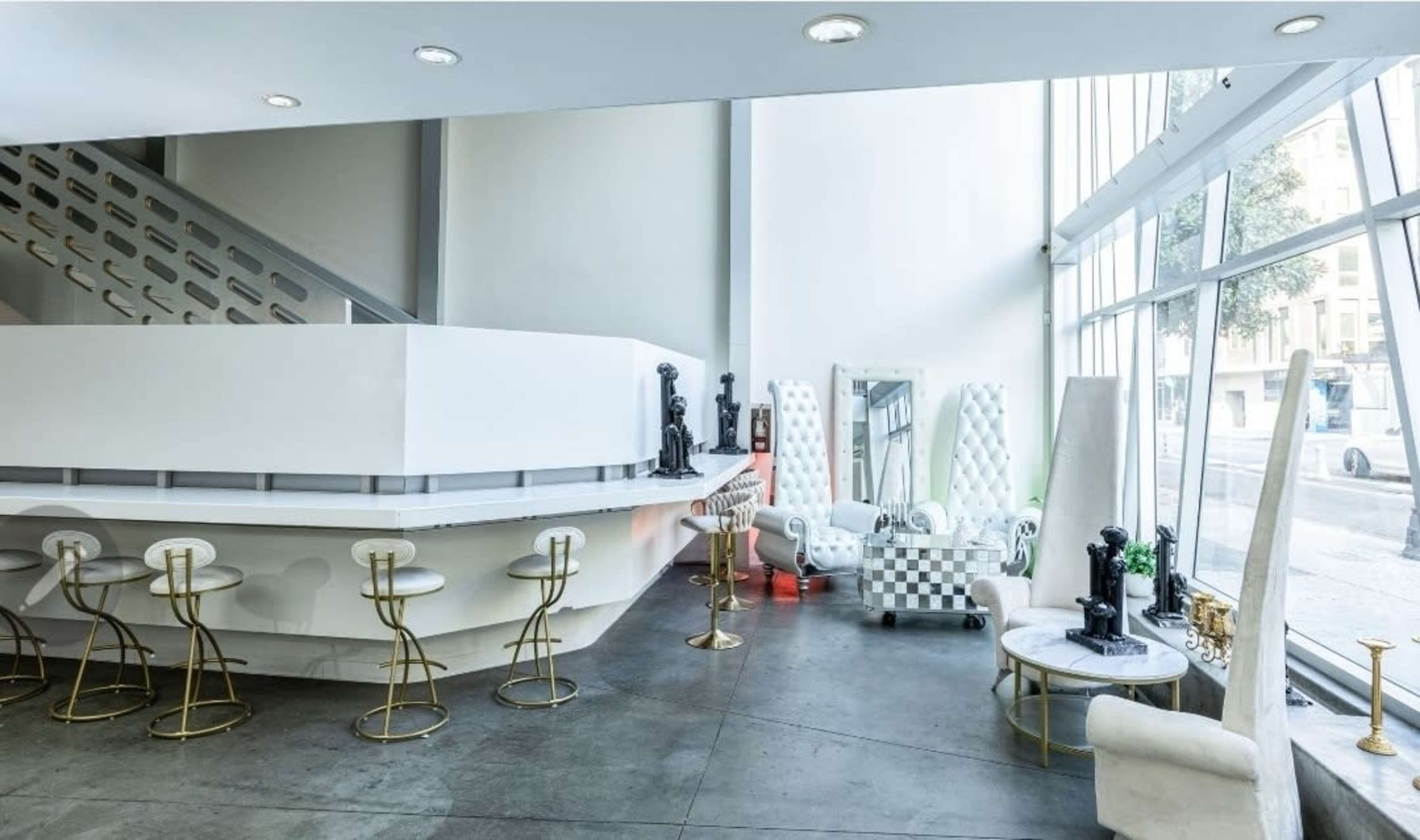 The image shows a modern interior space featuring a sleek bar area with gold-accented stools and an arrangement of unique furniture against large windows.