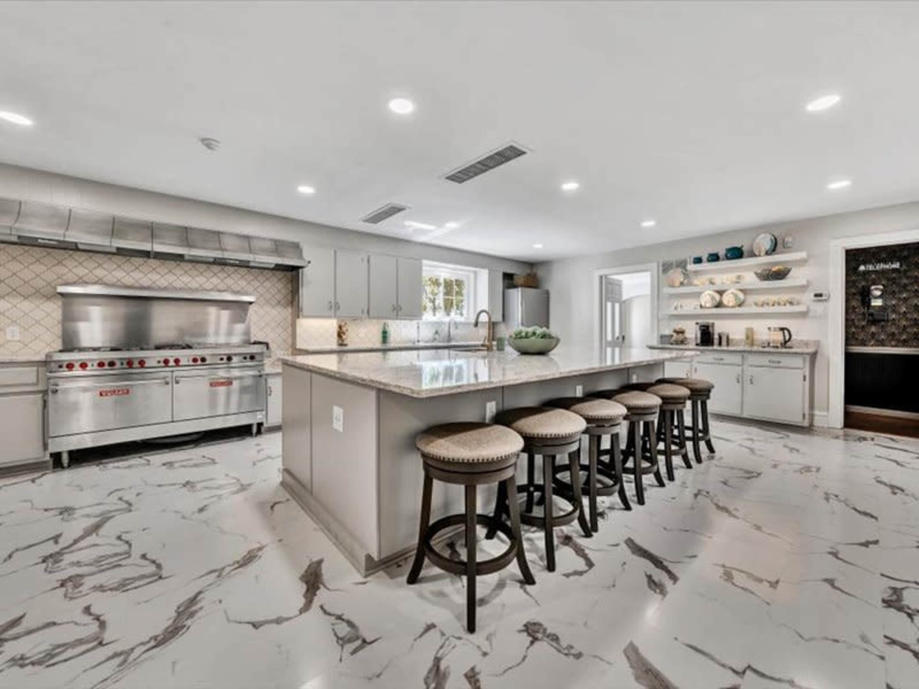 A modern kitchen features a large island with seating, stainless steel appliances, and marble flooring.