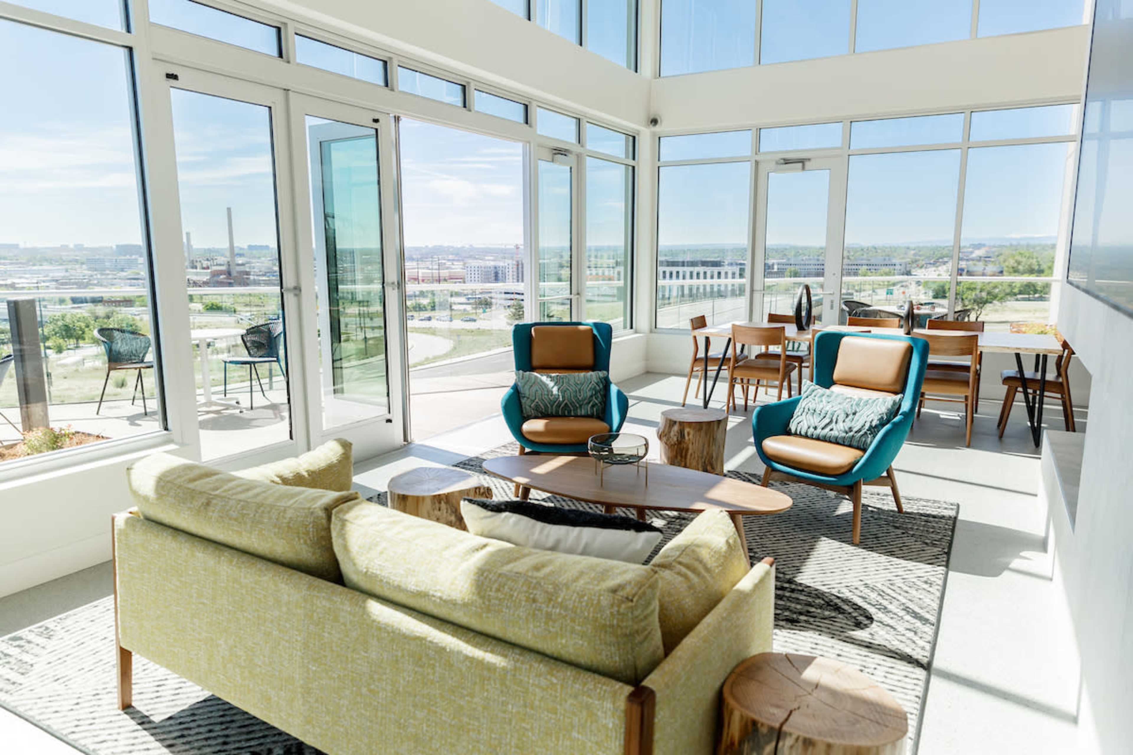 The image shows a modern lounge area with large windows, featuring two chairs and a sofa arranged around a coffee table with a view of the city.