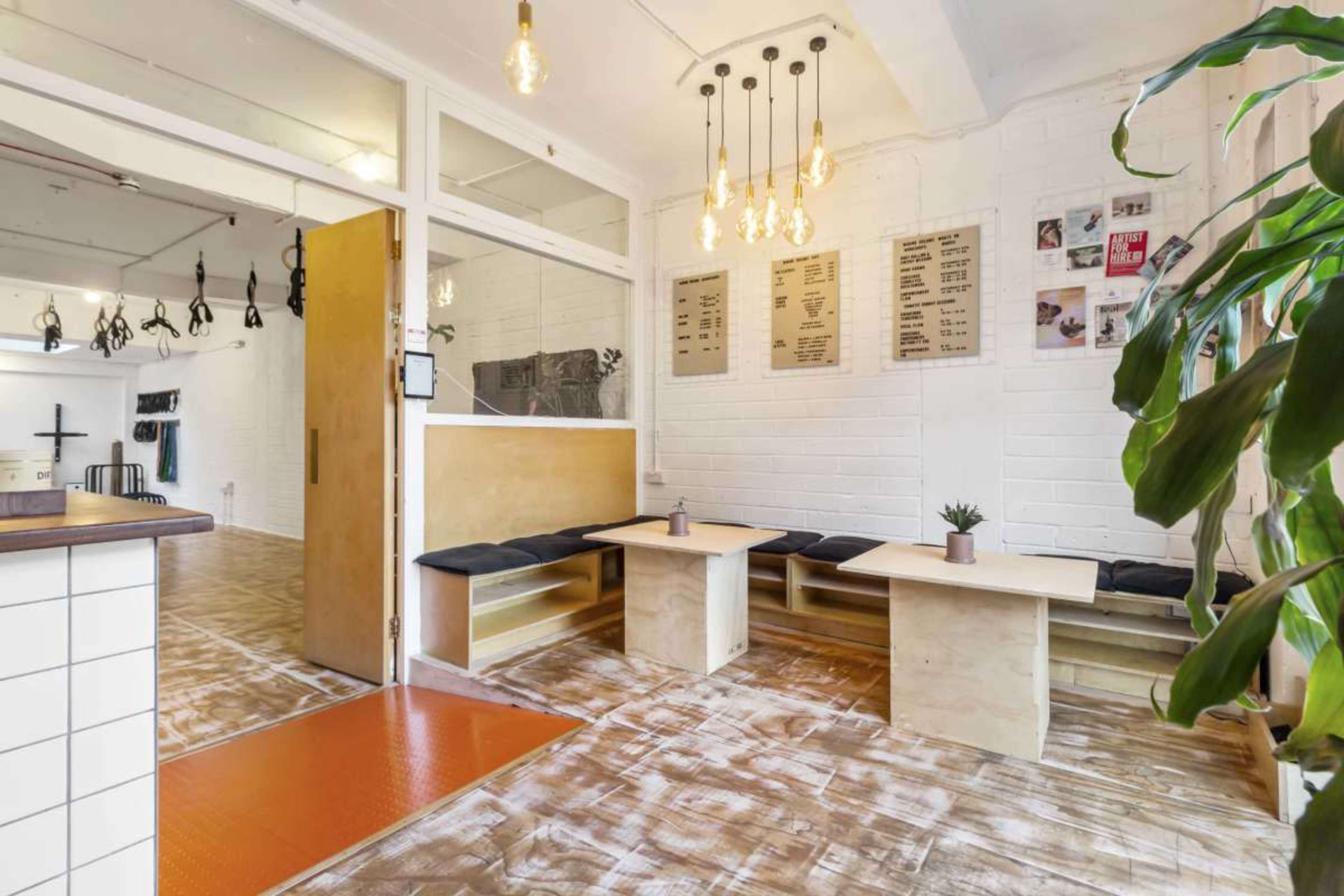 A modern interior space with wooden benches, tables, and pendant lighting, featuring a plant in the corner.