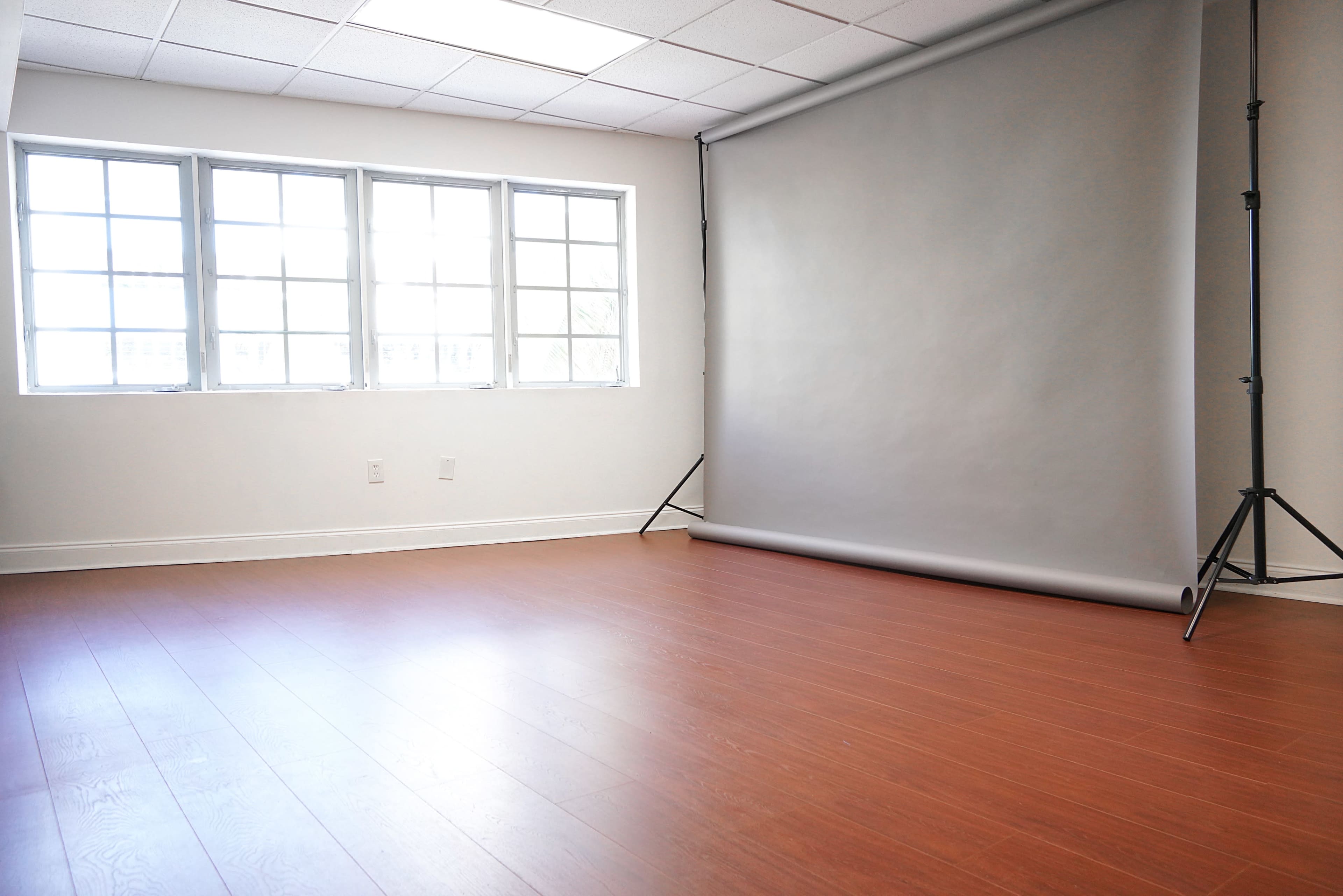 A photography studio with large windows, wooden flooring, and a gray backdrop set up against one wall.