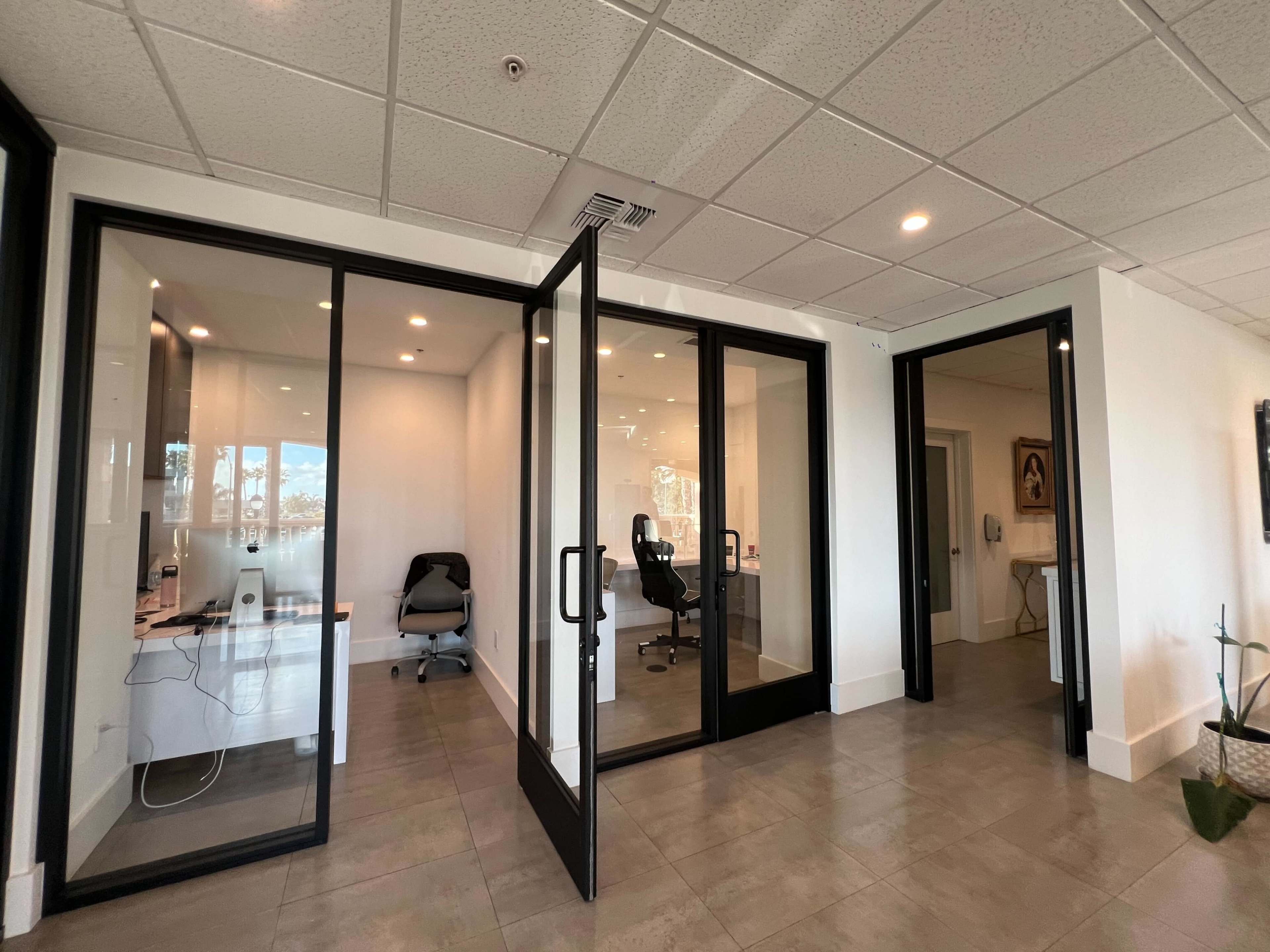 A modern office area with glass-walled meeting rooms and doors leading to another space.