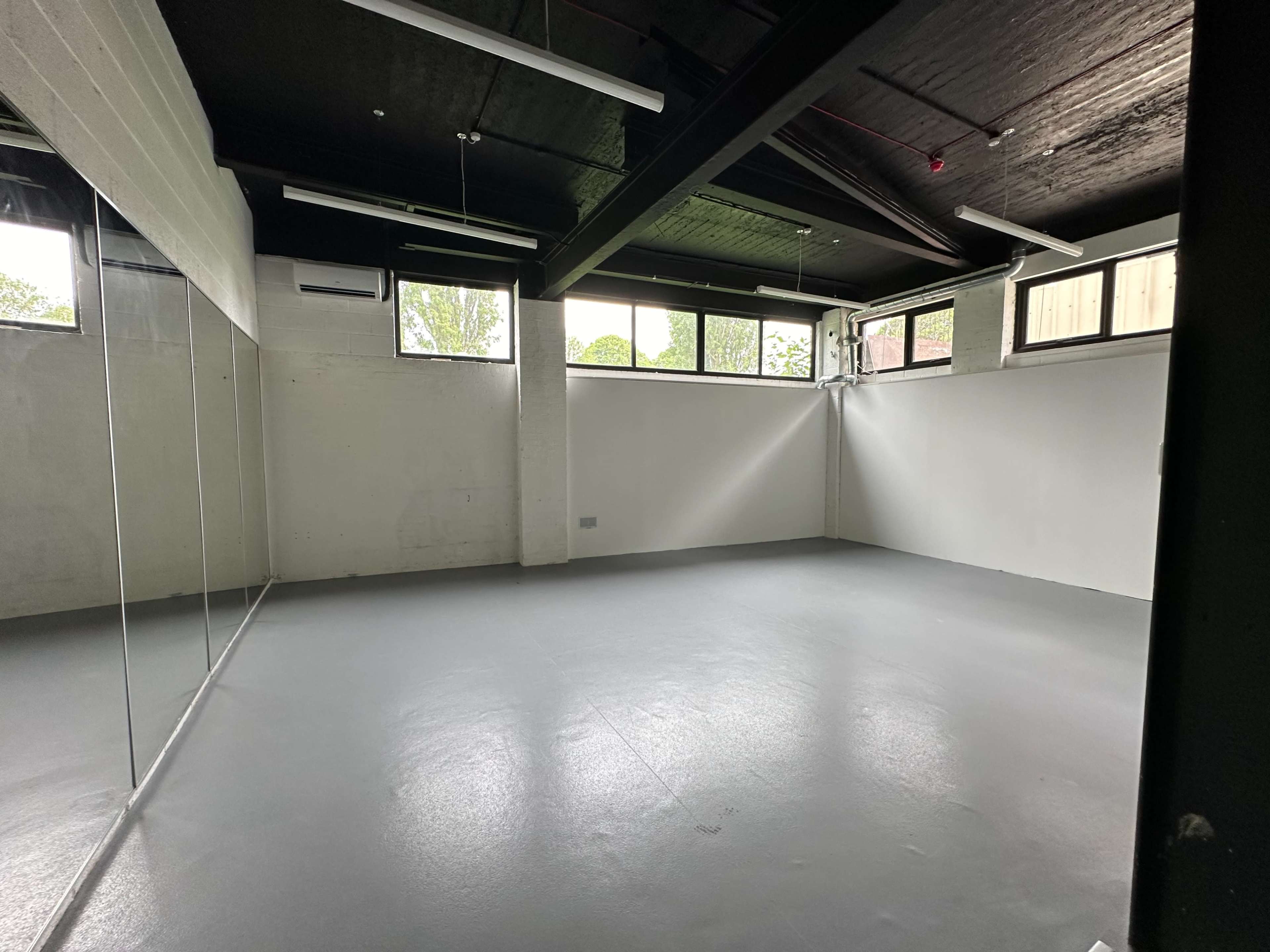 An empty room with large windows, a grey floor, and one wall featuring mirrors.