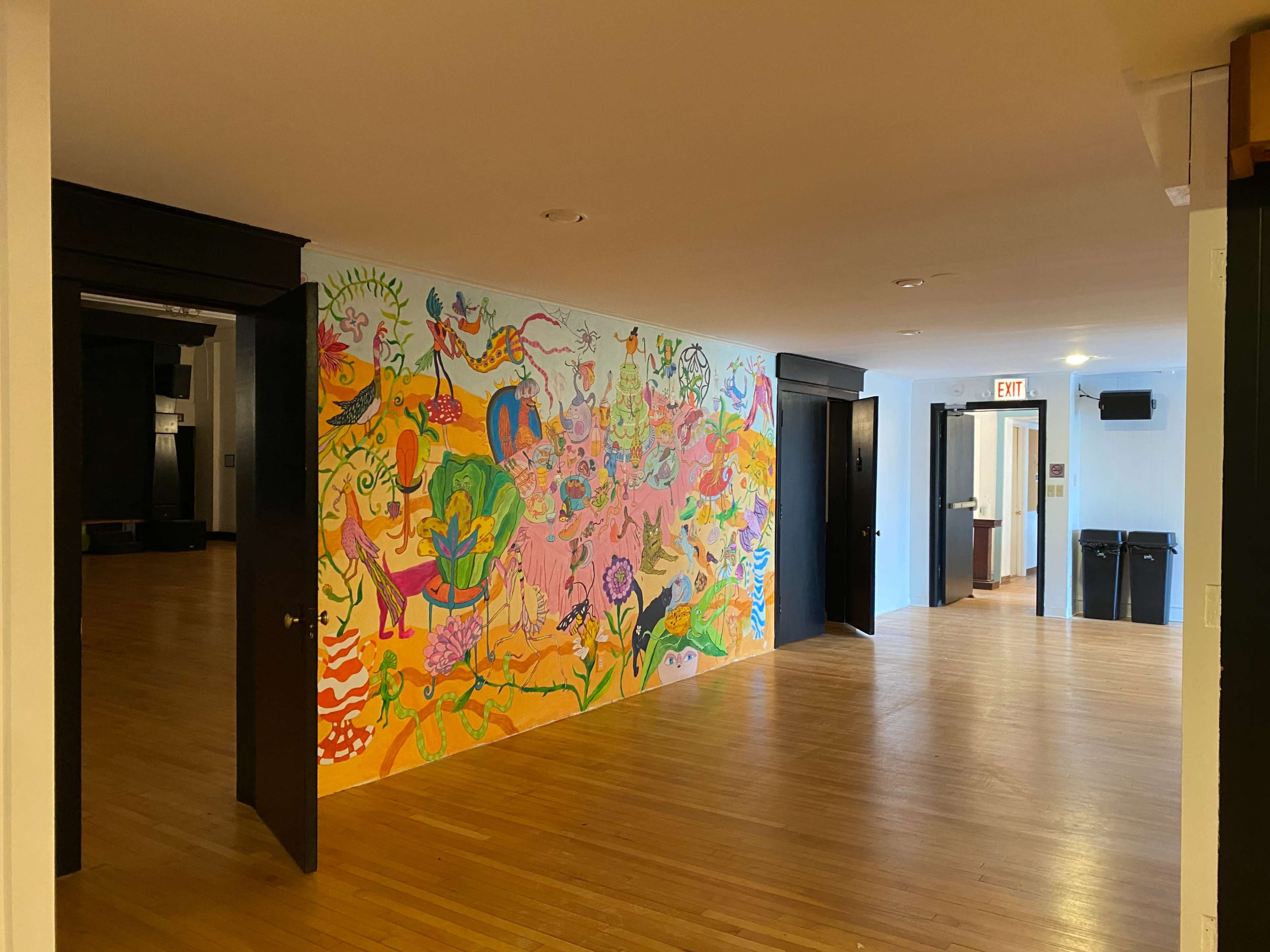 A hallway featuring a vibrant mural on one wall, with several doors leading to adjacent rooms and a glimpse of a kitchen area in the background.