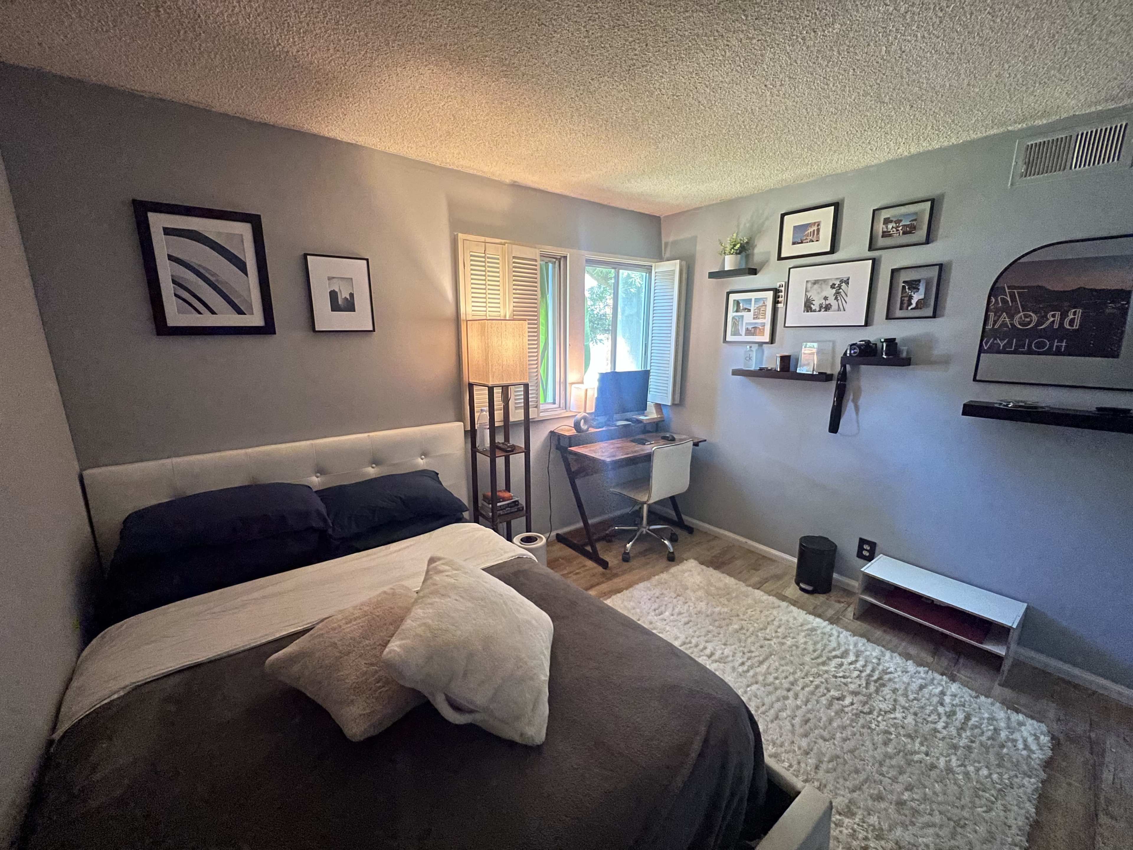 A small bedroom with a bed, a desk with a computer, and several framed pictures on the walls.