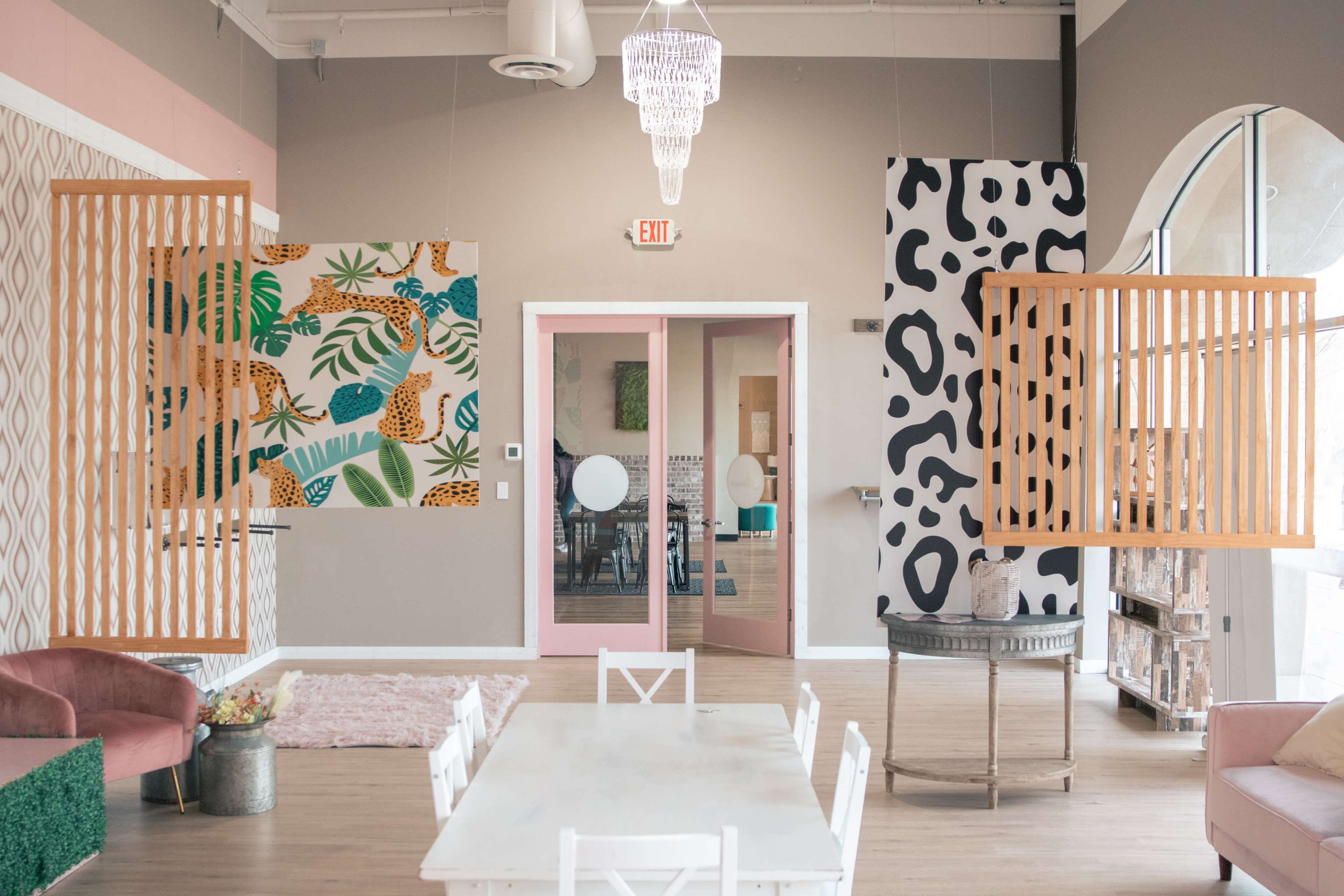 The image shows a brightly lit interior space featuring colorful wall murals, wooden partitions, and a dining table surrounded by chairs.