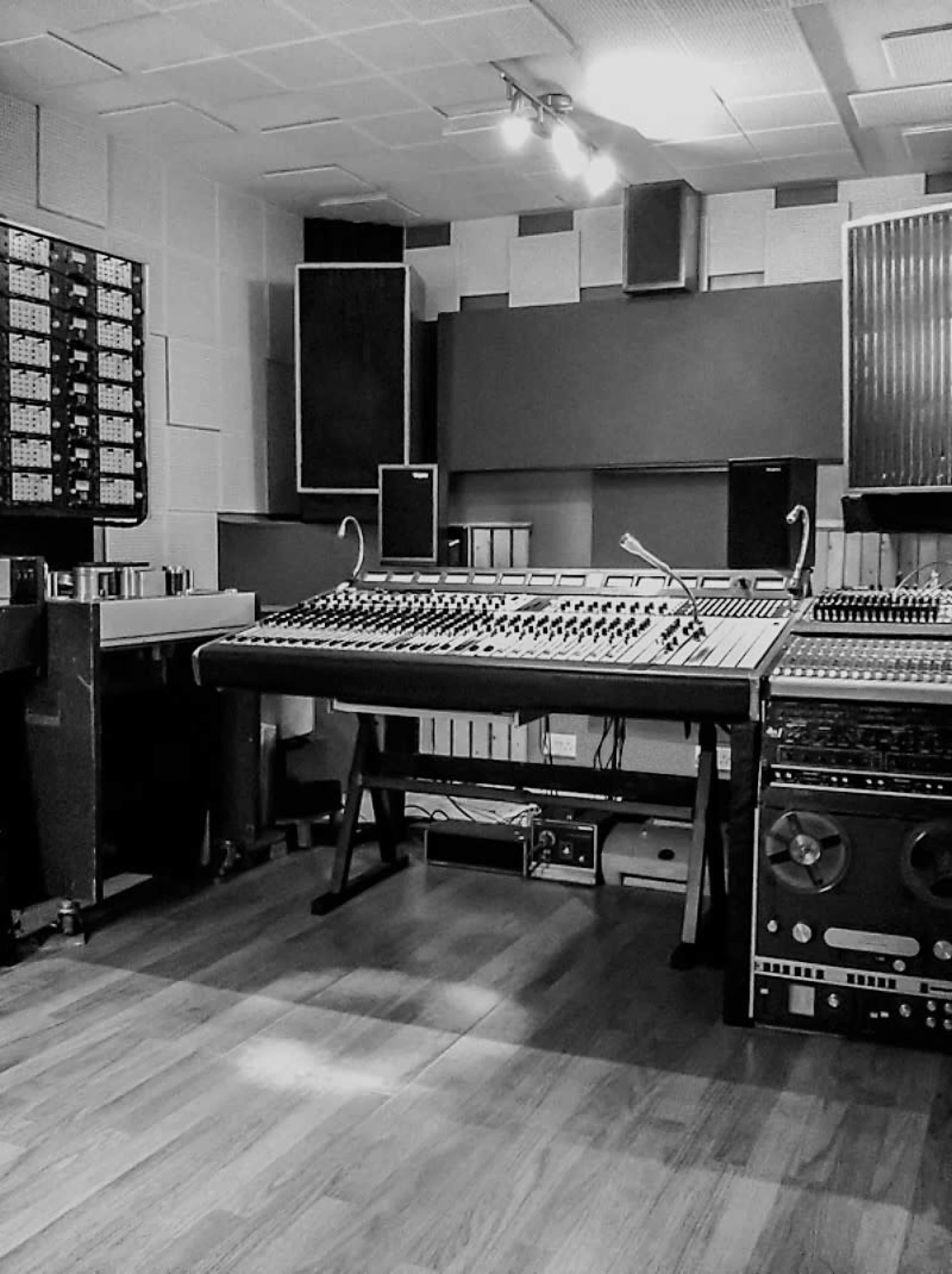 A music studio featuring a large mixing console, various audio equipment, and soundproofing panels on the walls.