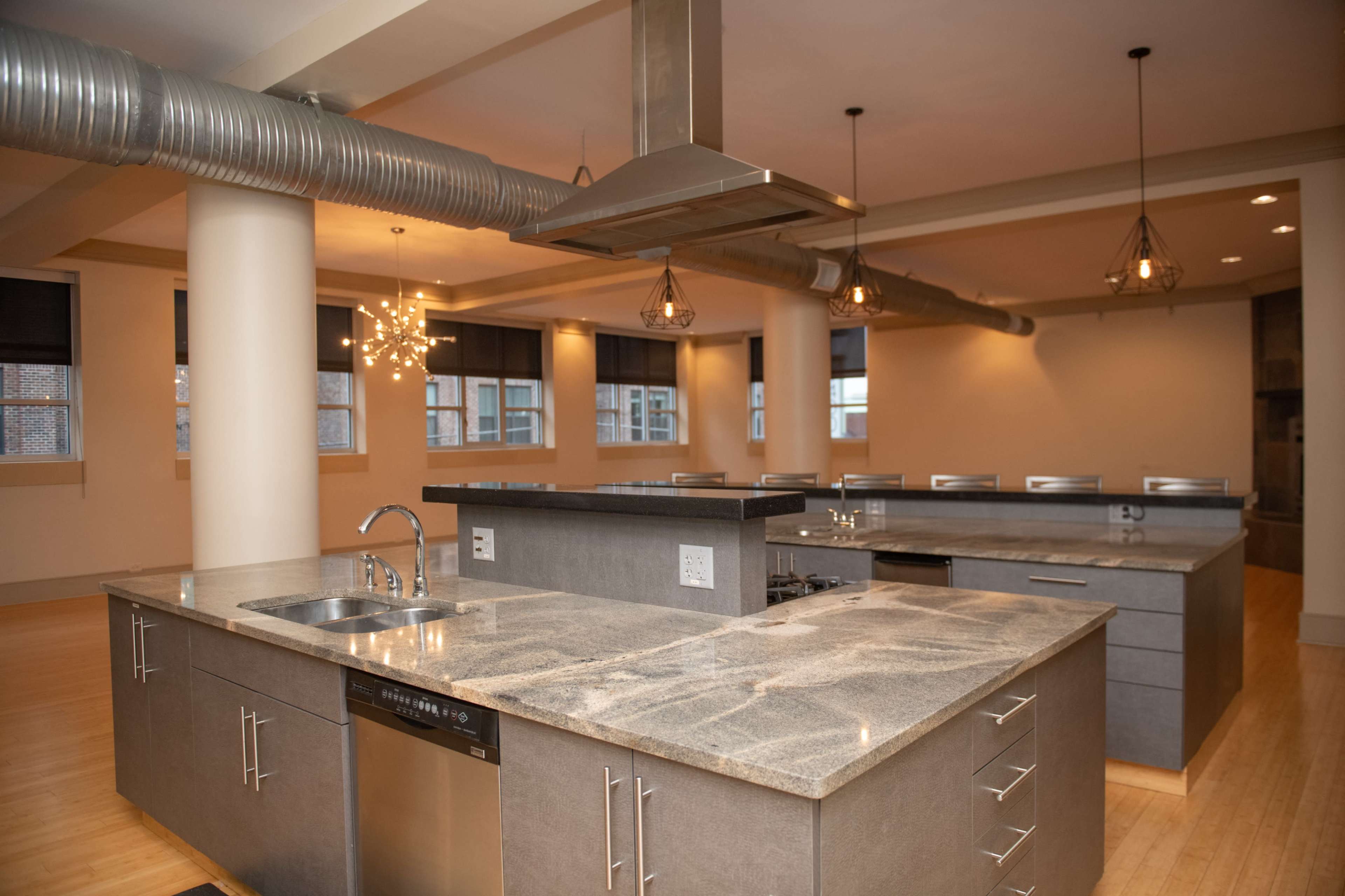 The image showcases a modern kitchen space featuring gray countertops, stainless steel appliances, and an open layout illuminated by pendant lights.