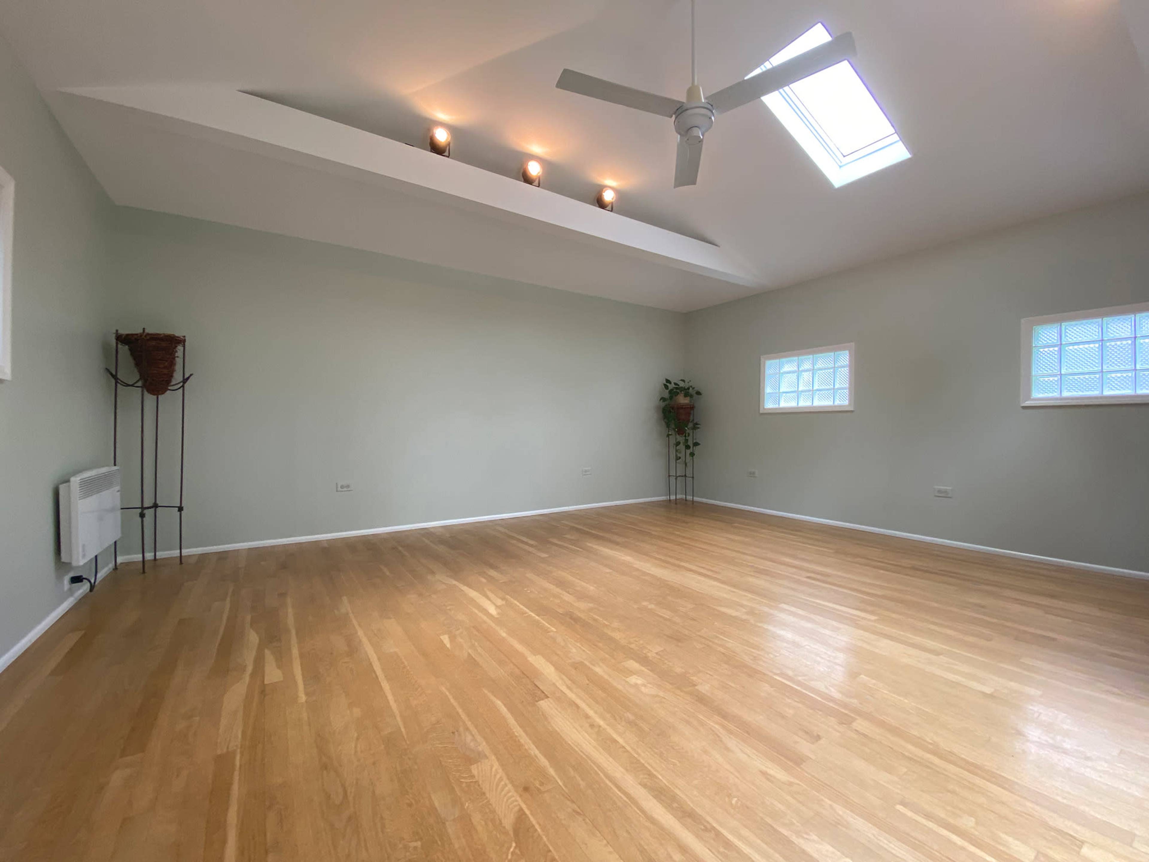 A spacious room with wooden flooring, a ceiling fan, and several skylights illuminating the area.