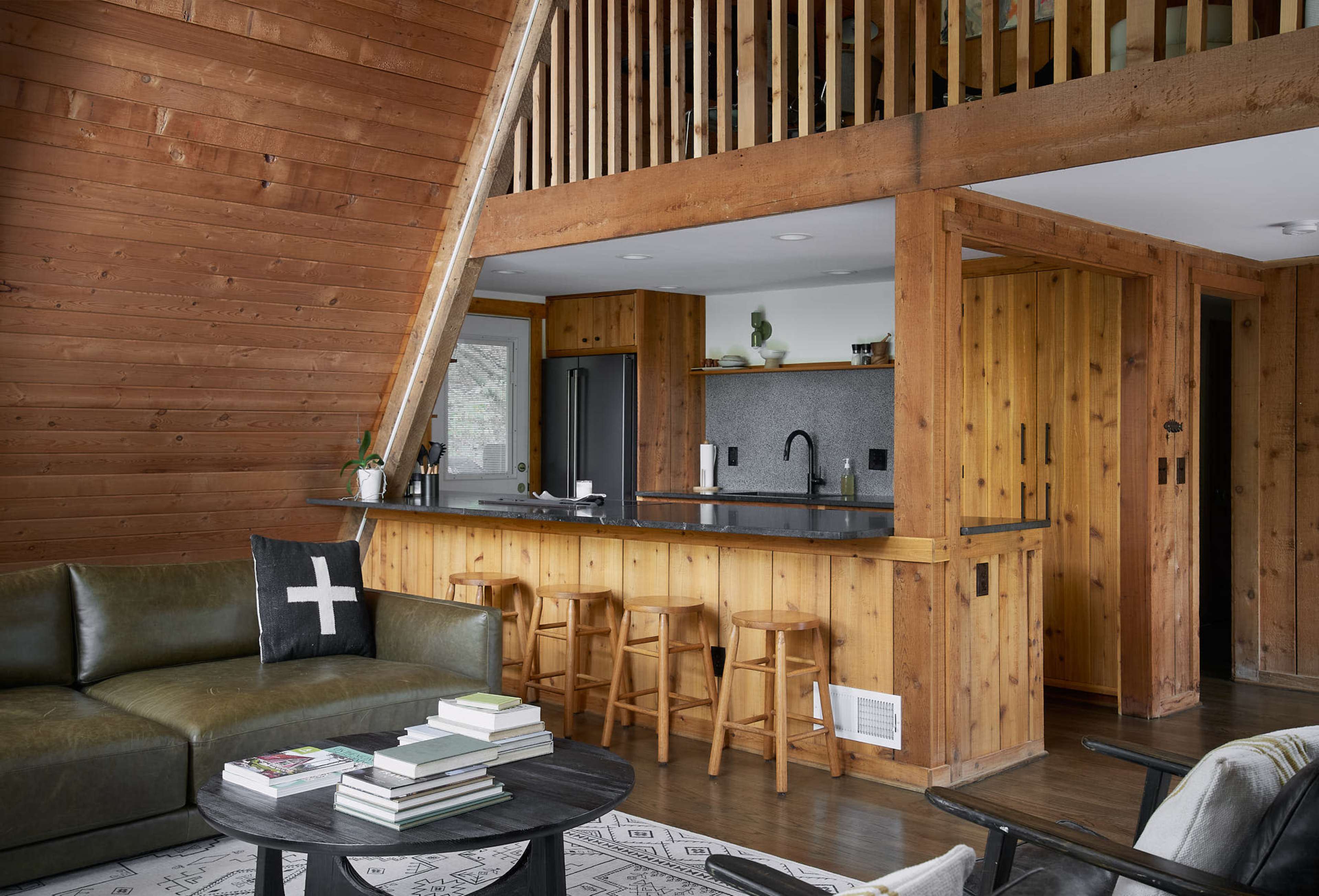 A modern cabin interior features wooden walls, a kitchen with bar seating, and a living area with a couch and coffee table.