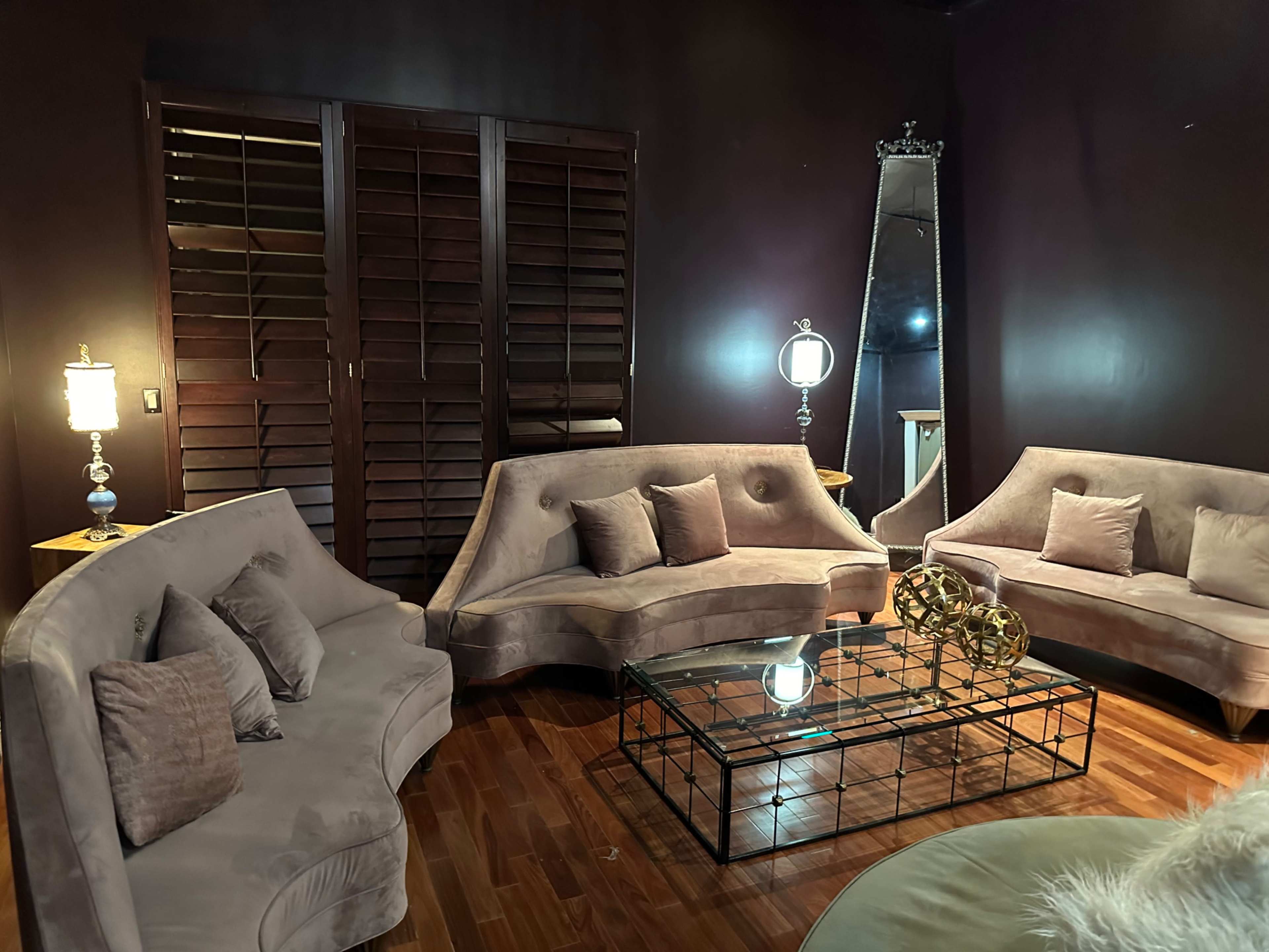 The image shows a dimly lit lounge area featuring three plush, curved sofas arranged around a glass coffee table.
