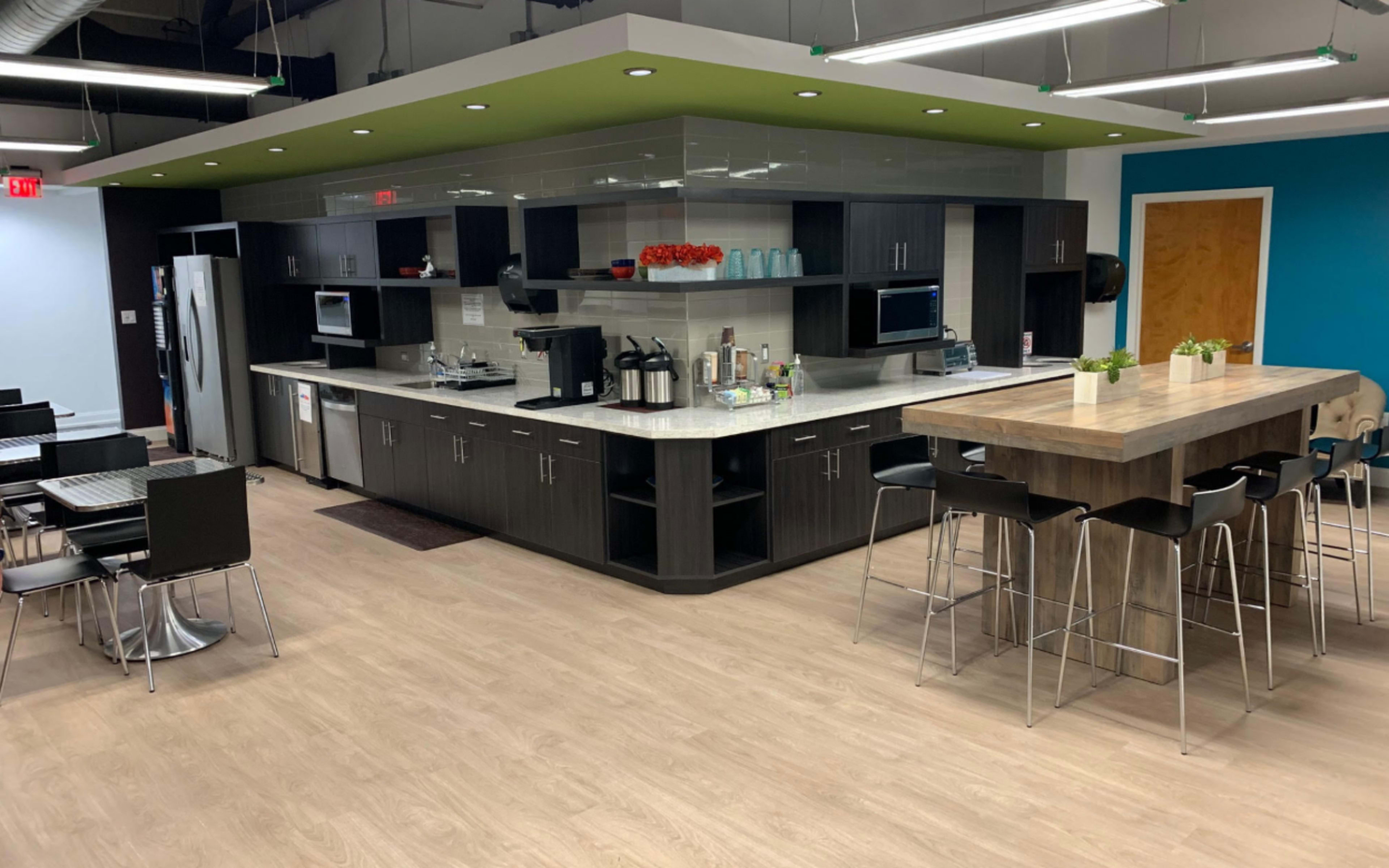 The image shows a modern kitchen area featuring a large central island, seating, and various appliances, all set against a backdrop of light wood flooring and colorful walls.
