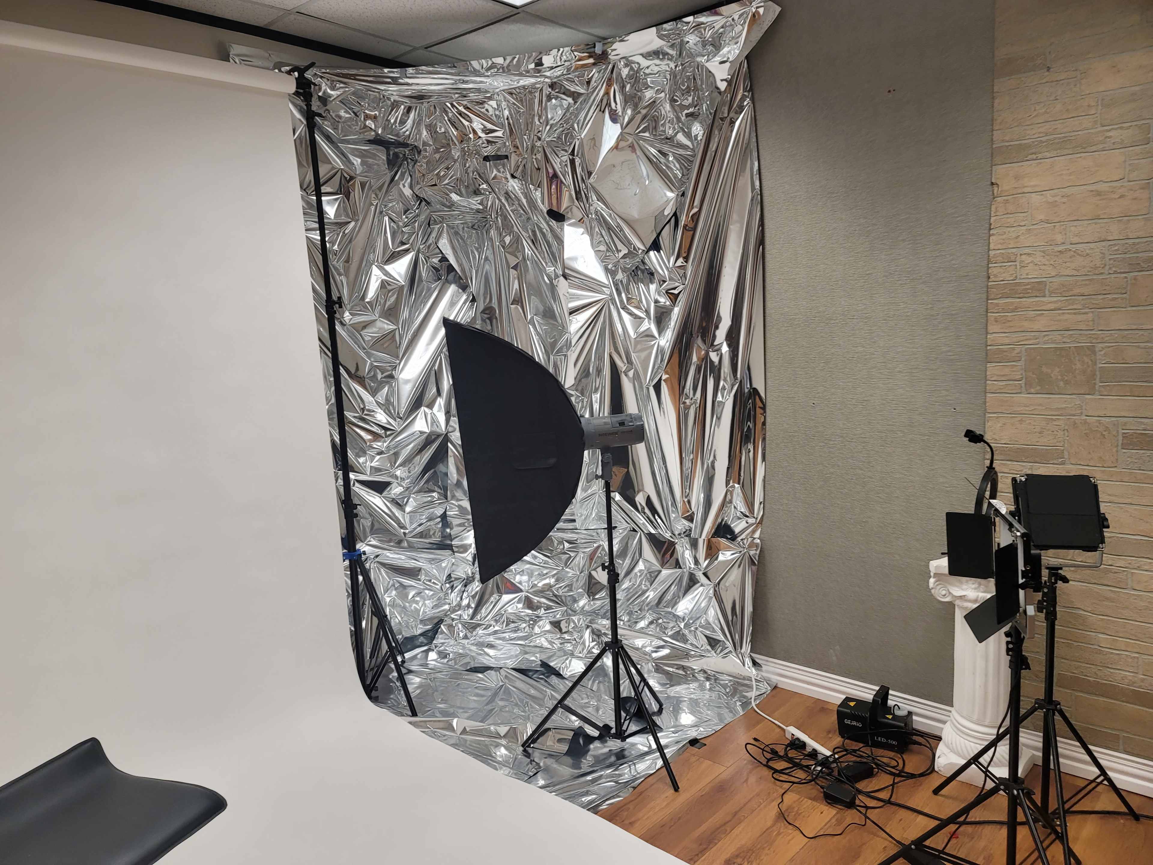 A photography studio setup featuring a shiny, reflective backdrop with lighting equipment on stands and a white backdrop to the side.