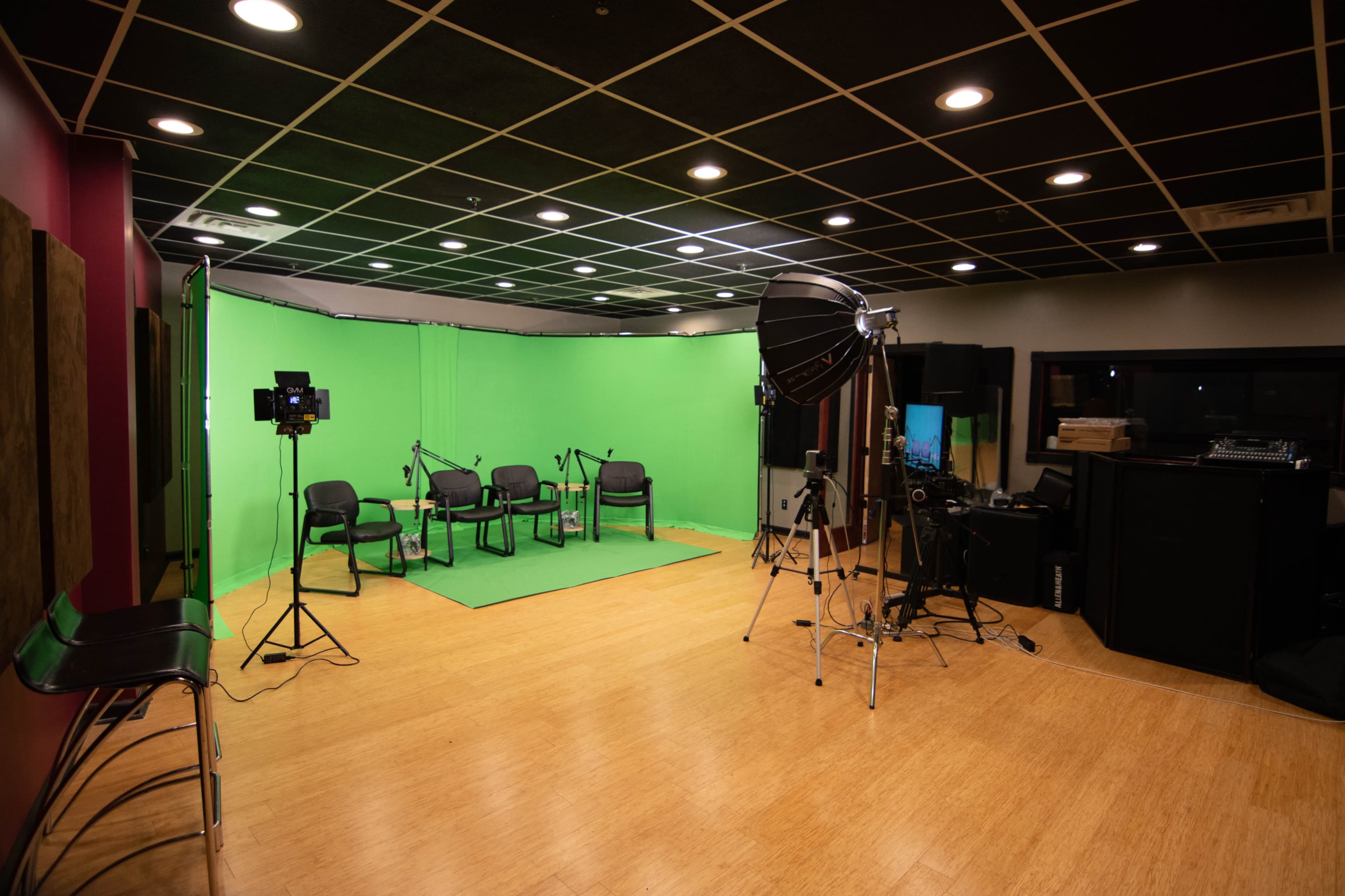The image depicts a recording studio featuring a green screen backdrop, several chairs, and various lighting equipment.