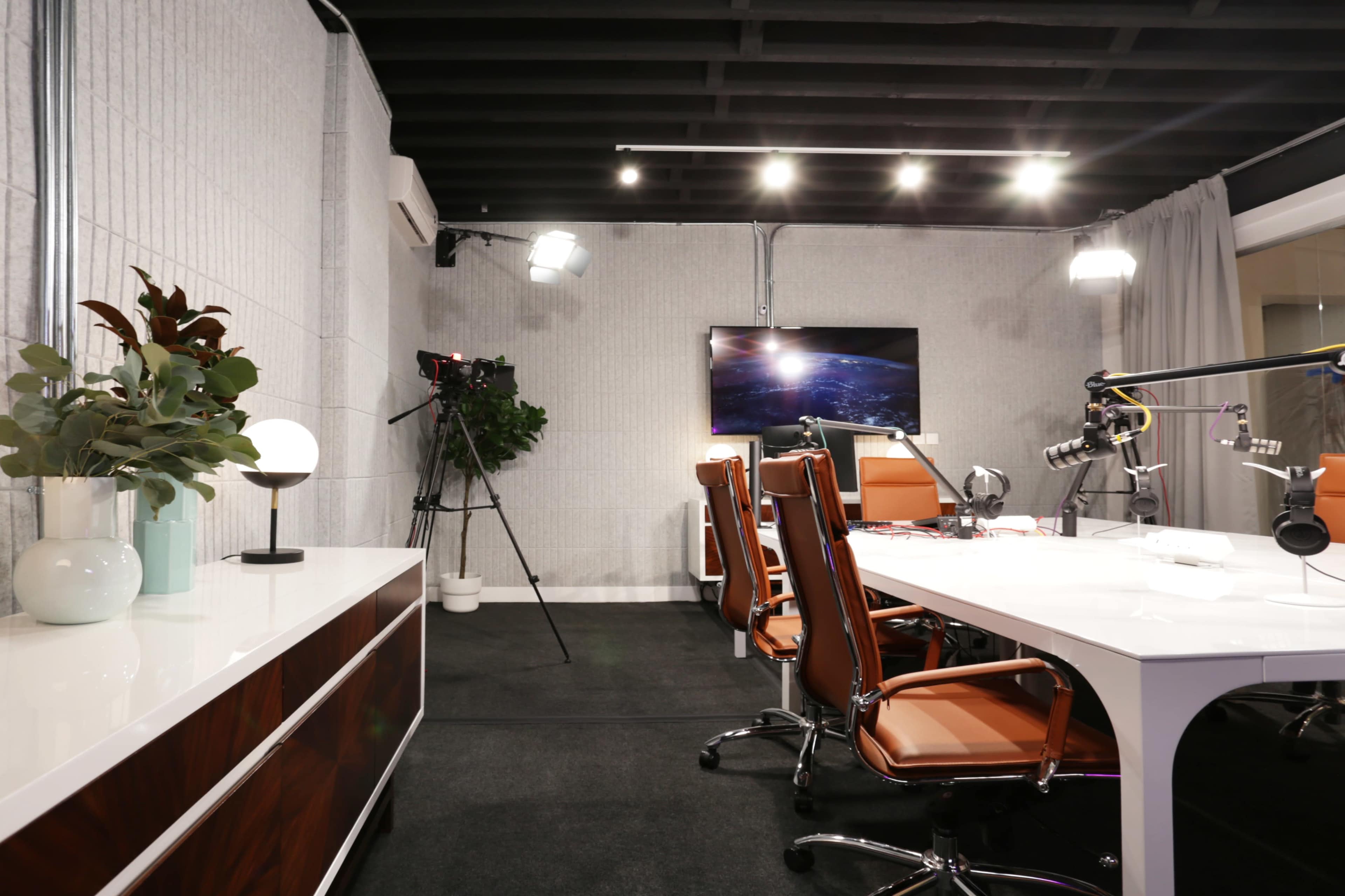 A modern conference room with a large white table, brown leather chairs, and media equipment set up for recording.
