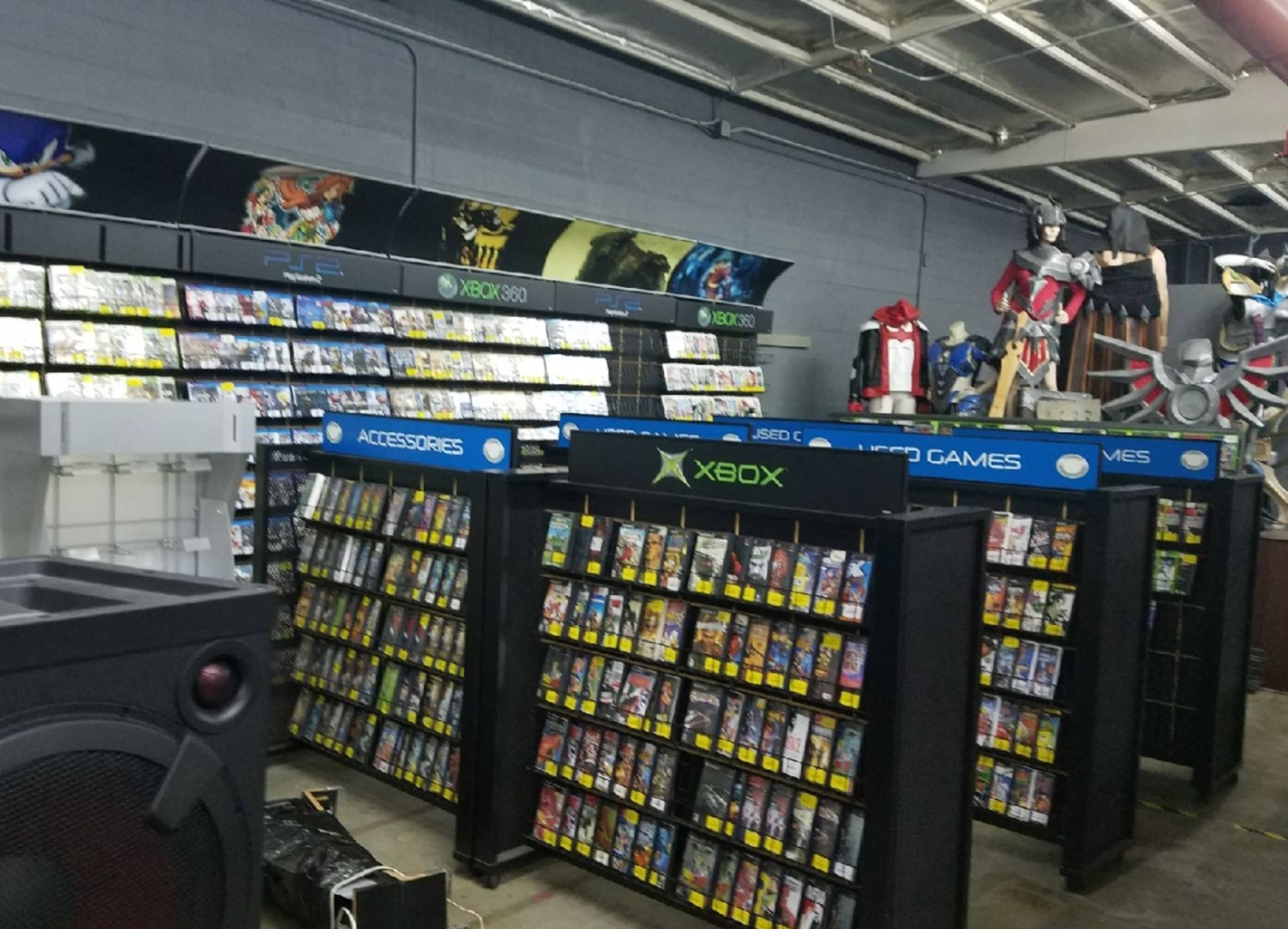 A retail store aisle with shelves filled with various video games, including sections for Xbox and PlayStation titles, alongside gaming accessories and merchandise.