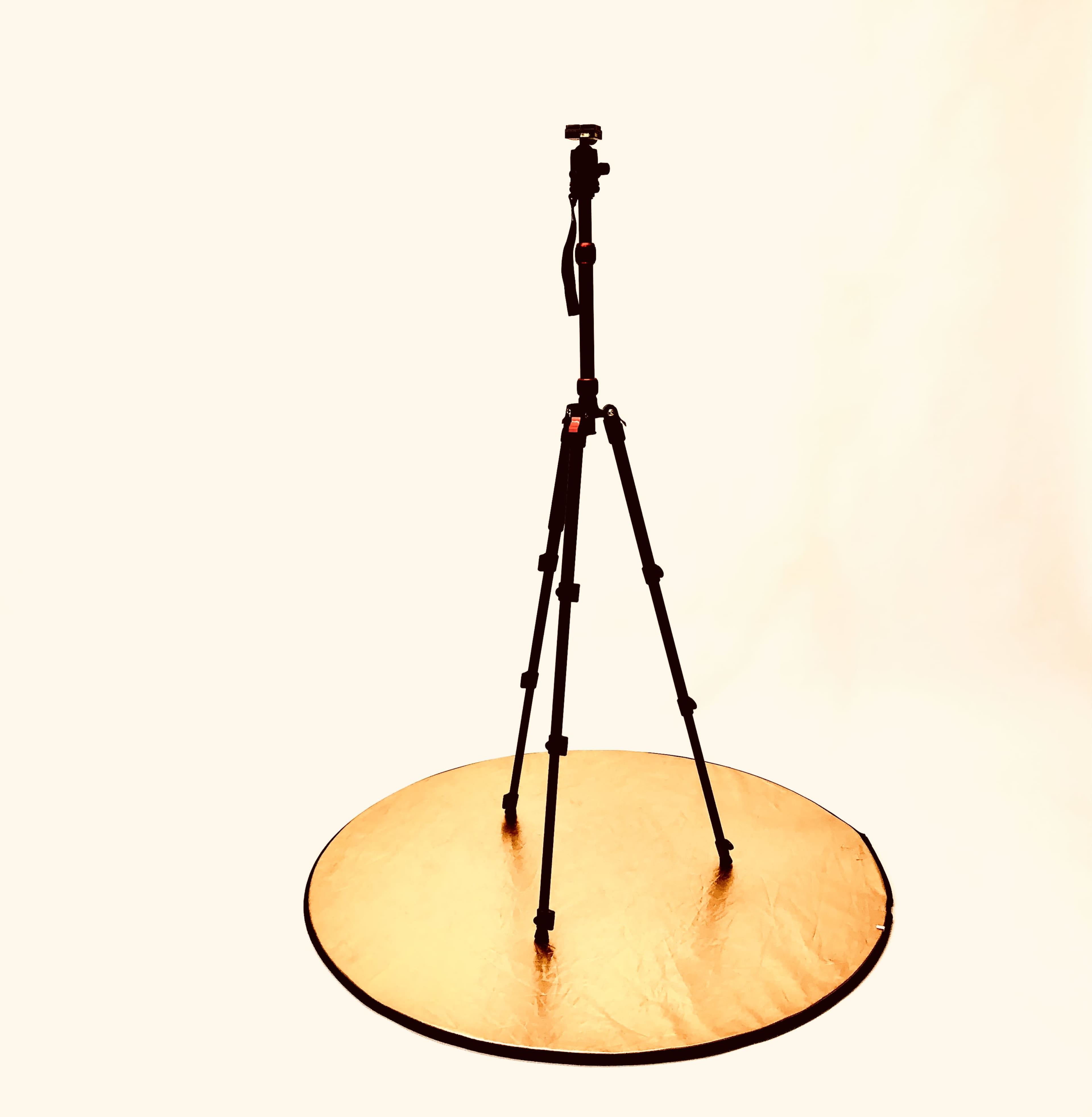 A black tripod stands on a circular, golden reflector against a light background.