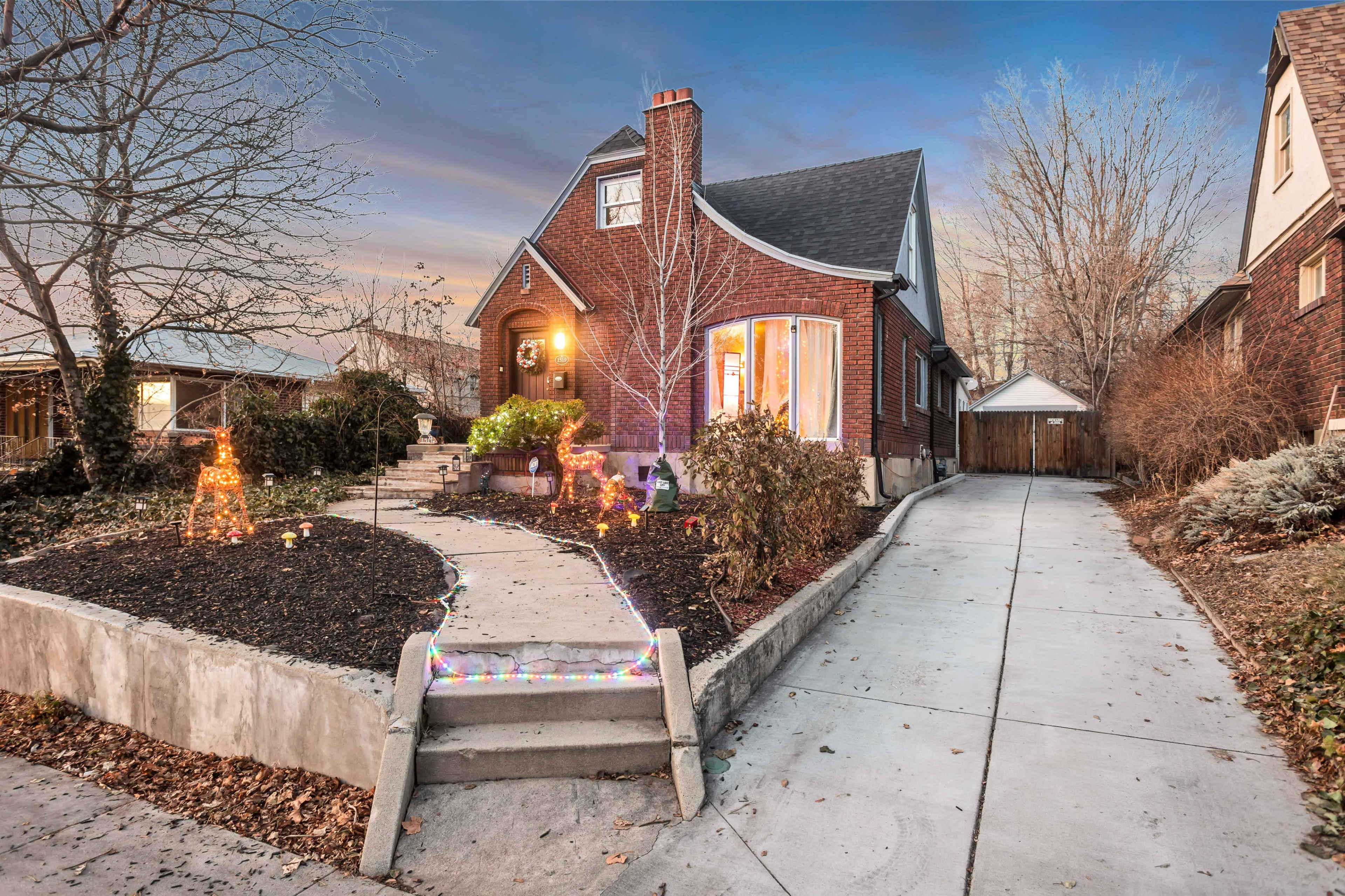 A brick house with a curved front window, surrounded by landscaped gardens and a driveway leading to a side gate.
