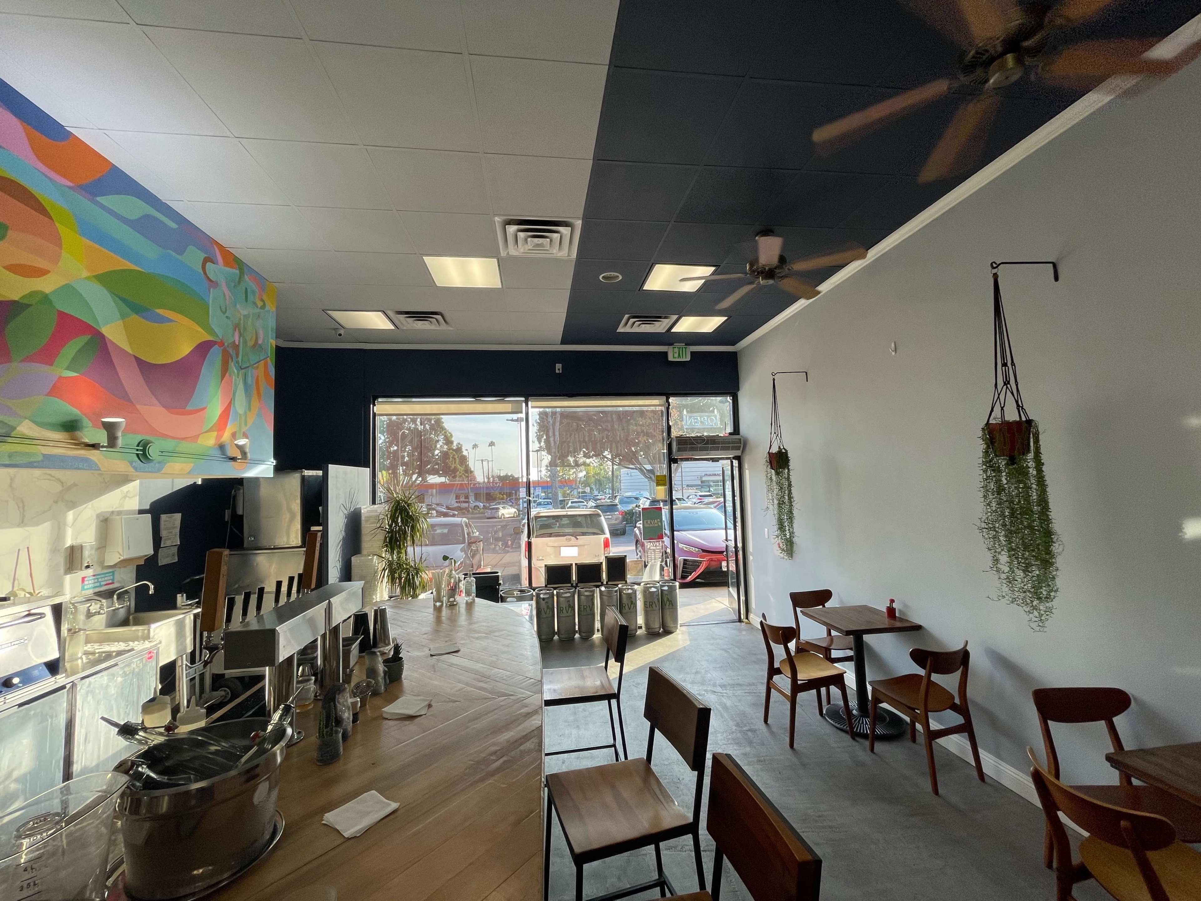 A modern café interior with a colorful mural, wooden tables, and a large window displaying outdoor scenery.