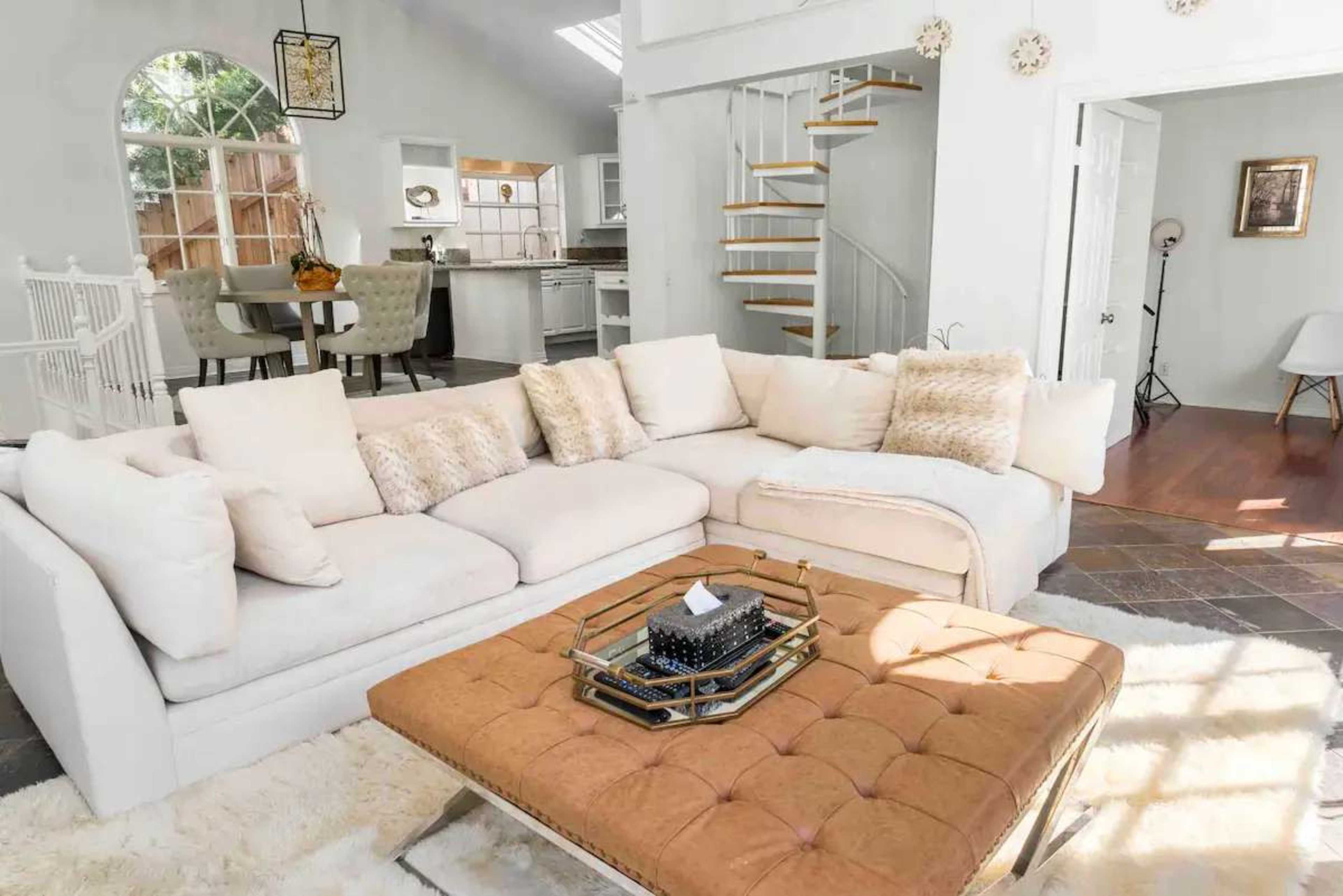 A light-filled living room featuring a large sectional sofa, a tufted coffee table, and a staircase leading to an upper level.