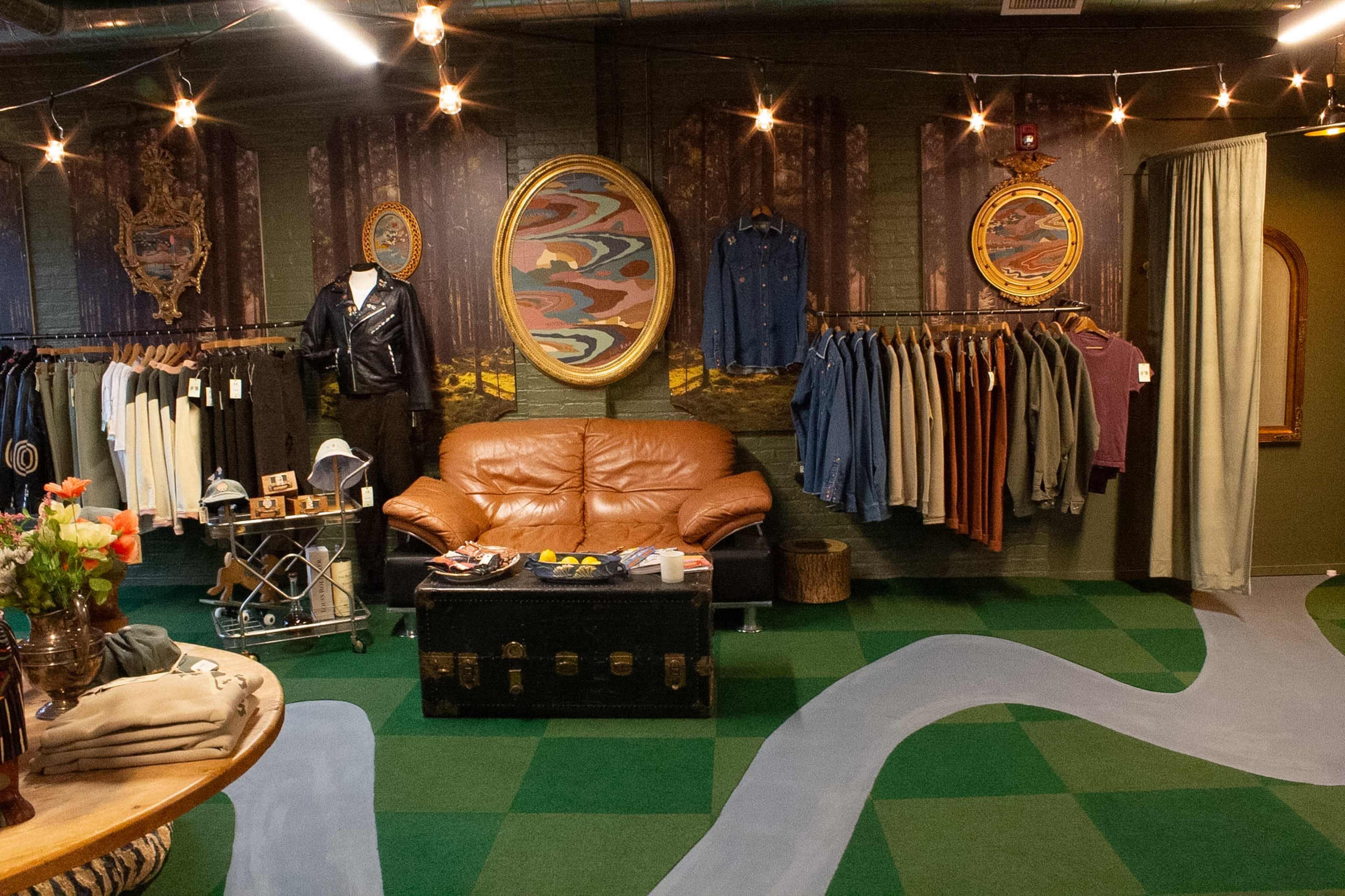 The image shows a boutique clothing store with racks of garments, a leather couch, and decorative art pieces on the walls.