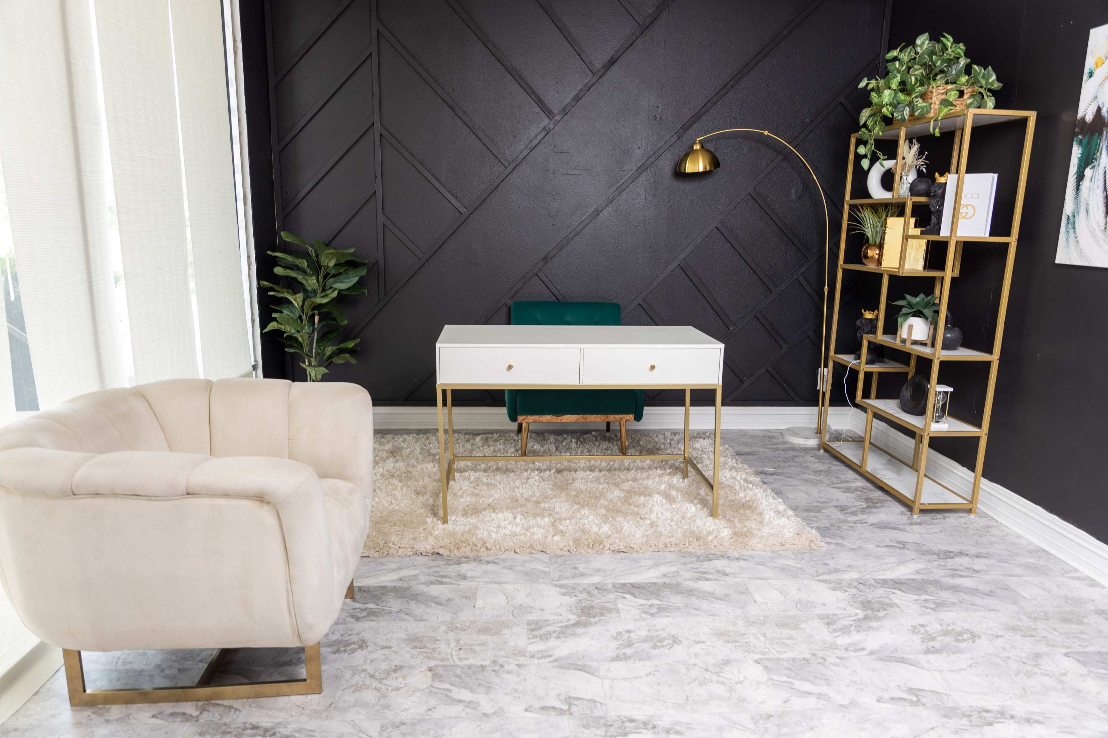 The image shows a modern office space featuring a white desk with gold accents, a green chair, a beige armchair, a textured rug, and a metal shelving unit against a black accent wall.