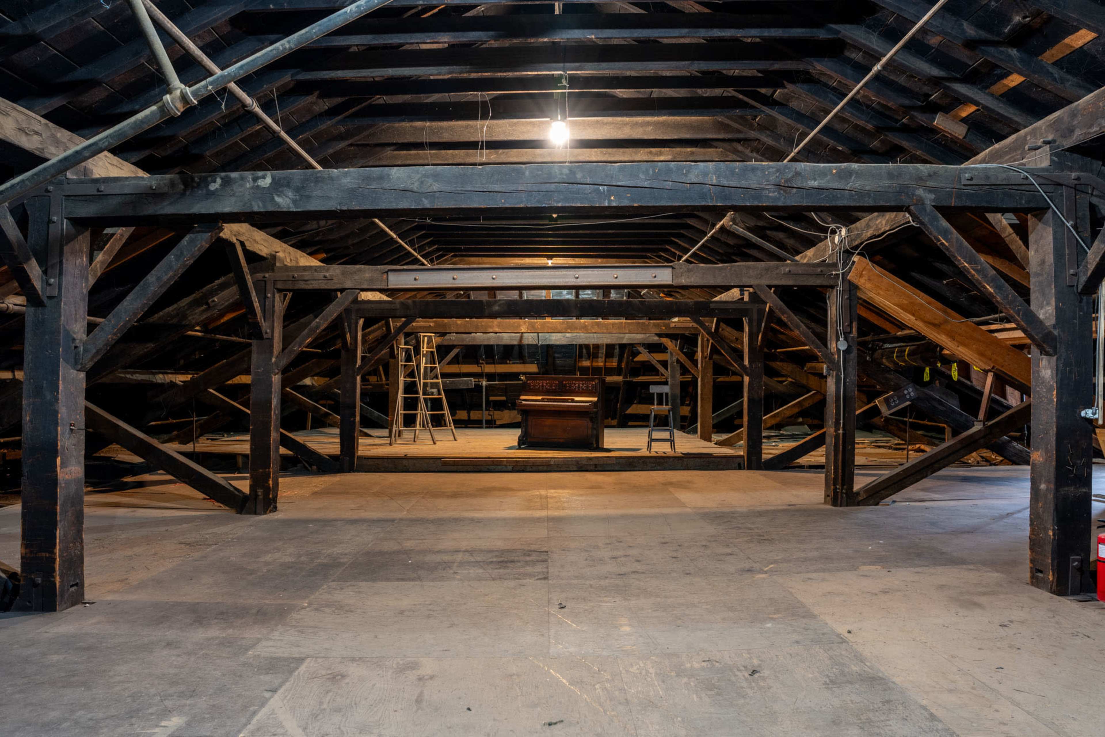 A spacious attic with exposed wooden beams, a wooden chest in the center, and two ladders leaning against the walls.
