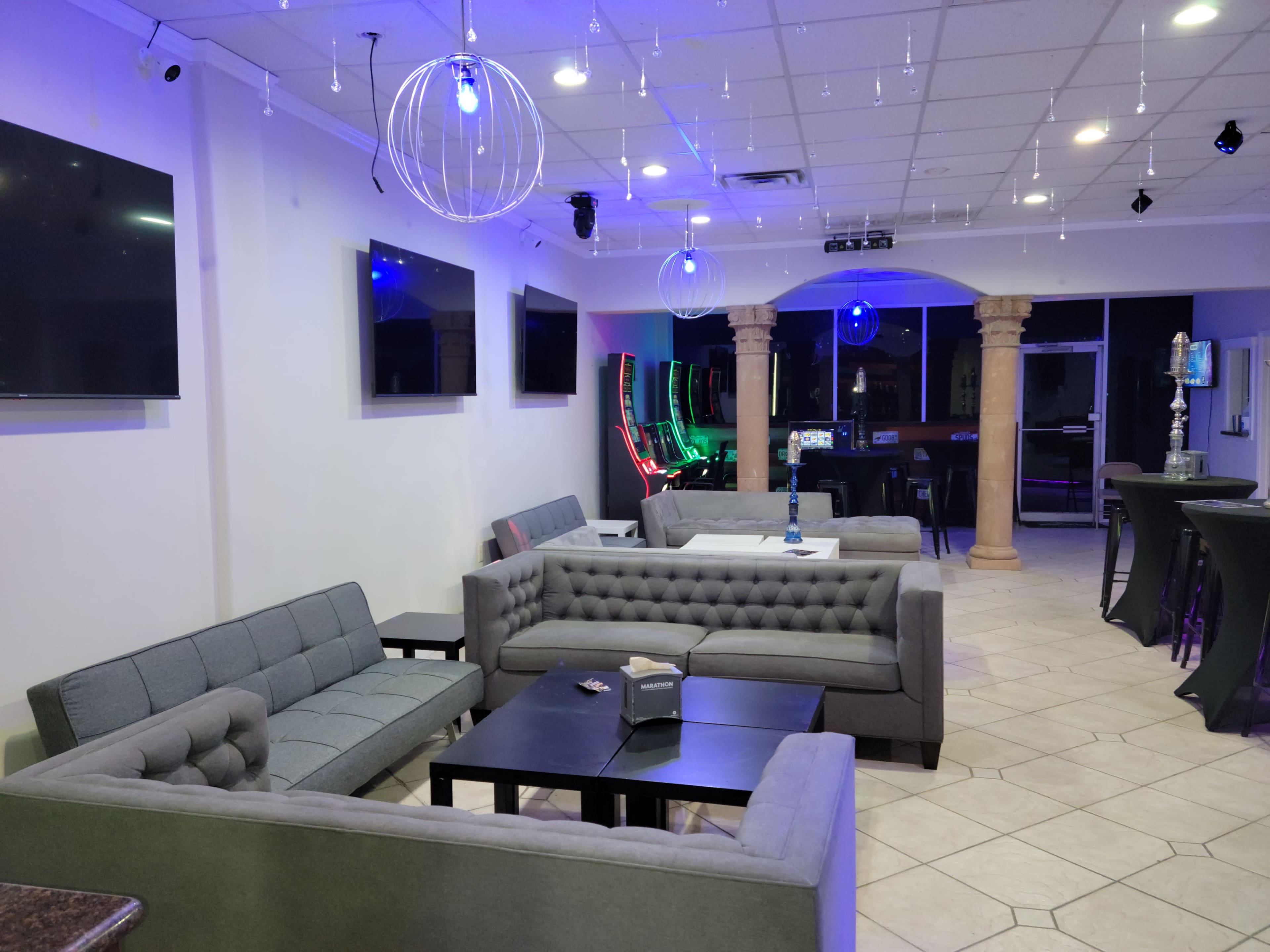 A modern lounge area with gray couches, a dark table, and multiple televisions on the walls.