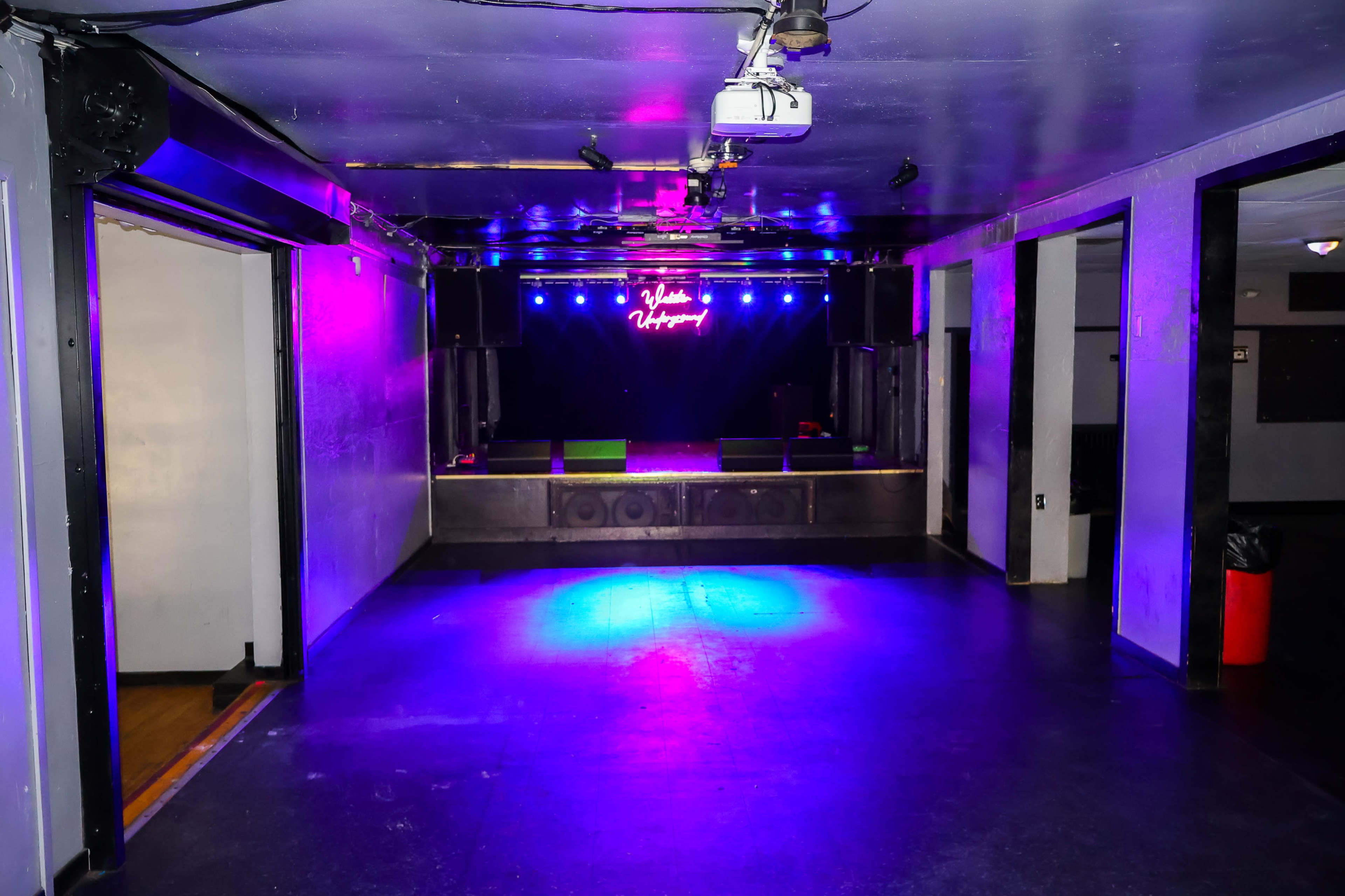 An empty performance space features a stage illuminated by colorful lights and a "Welcome" sign.