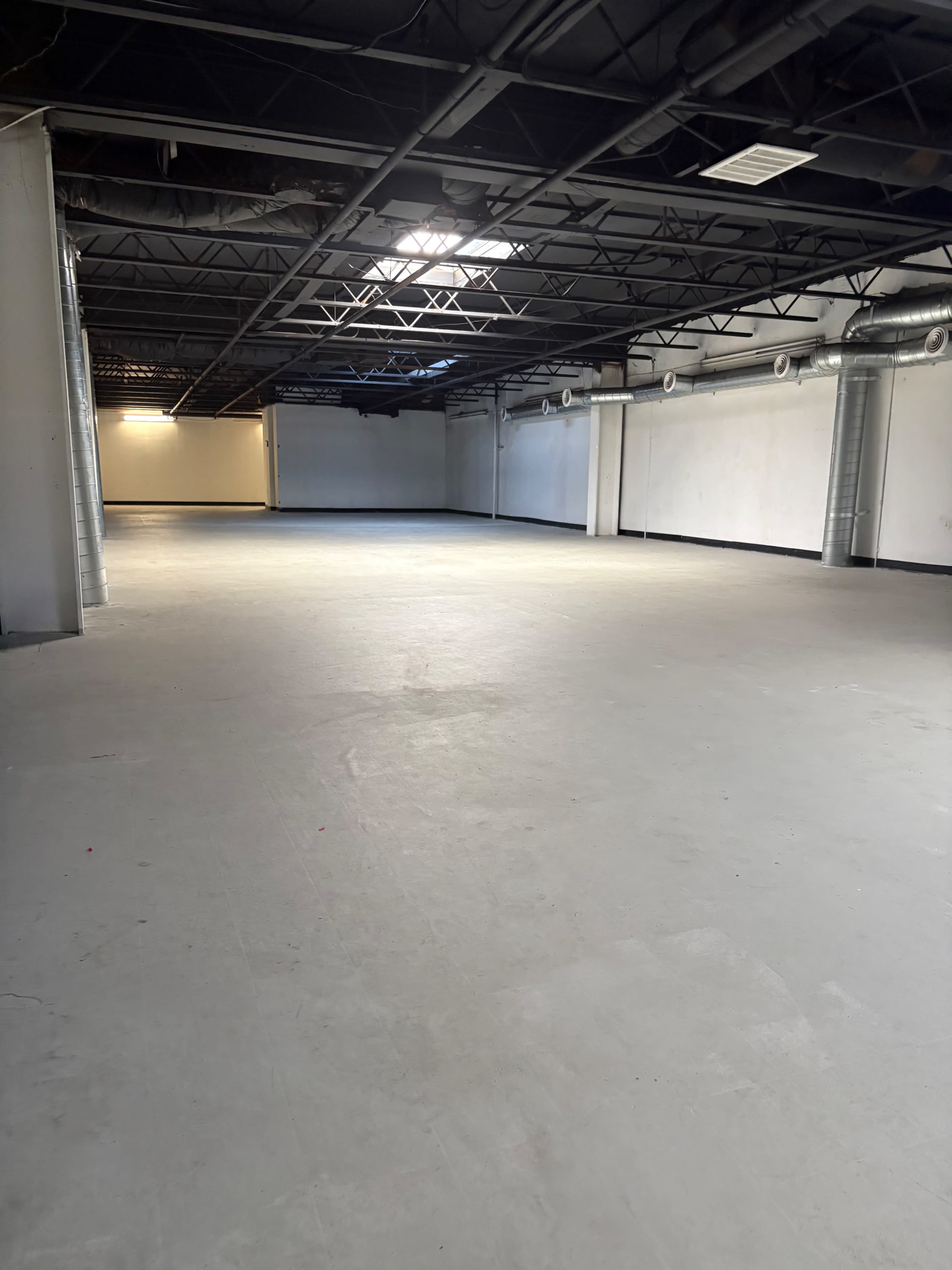 The image shows a large, empty warehouse space with exposed beams and ductwork on the ceiling.
