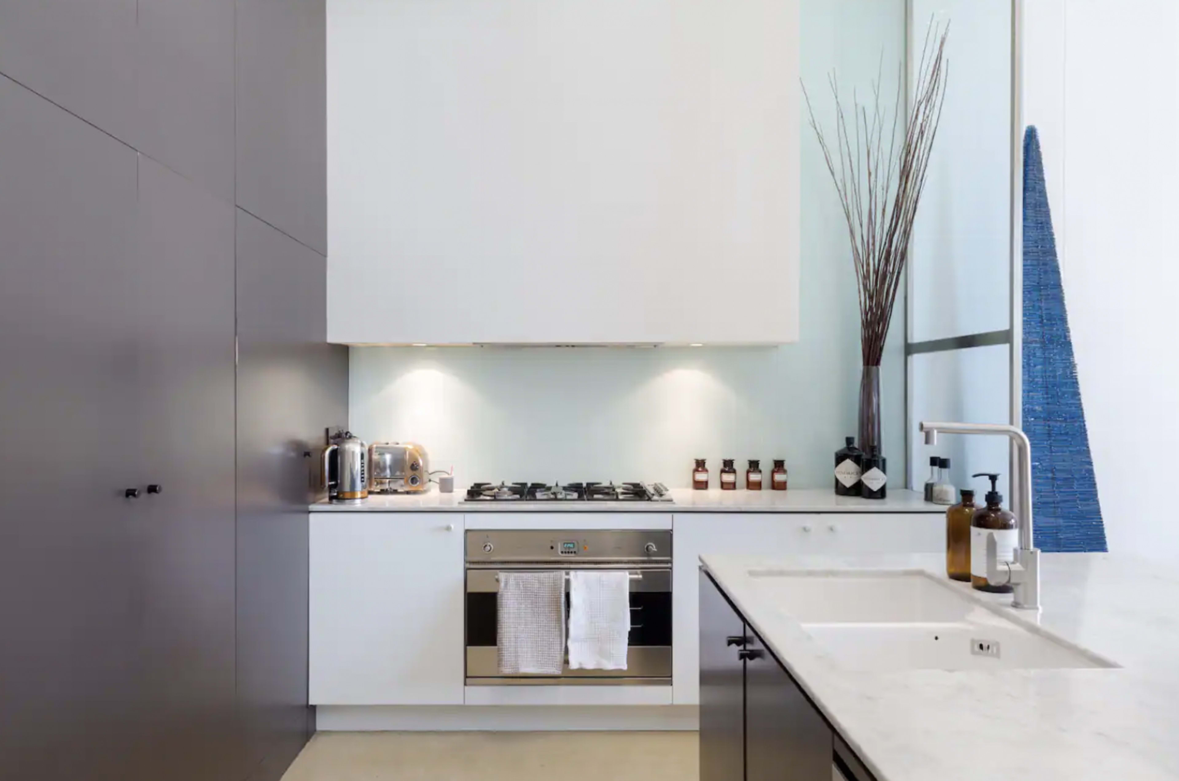 The image shows a modern kitchen with a stainless steel stove, minimalist cabinetry, and a sink with a marble countertop.