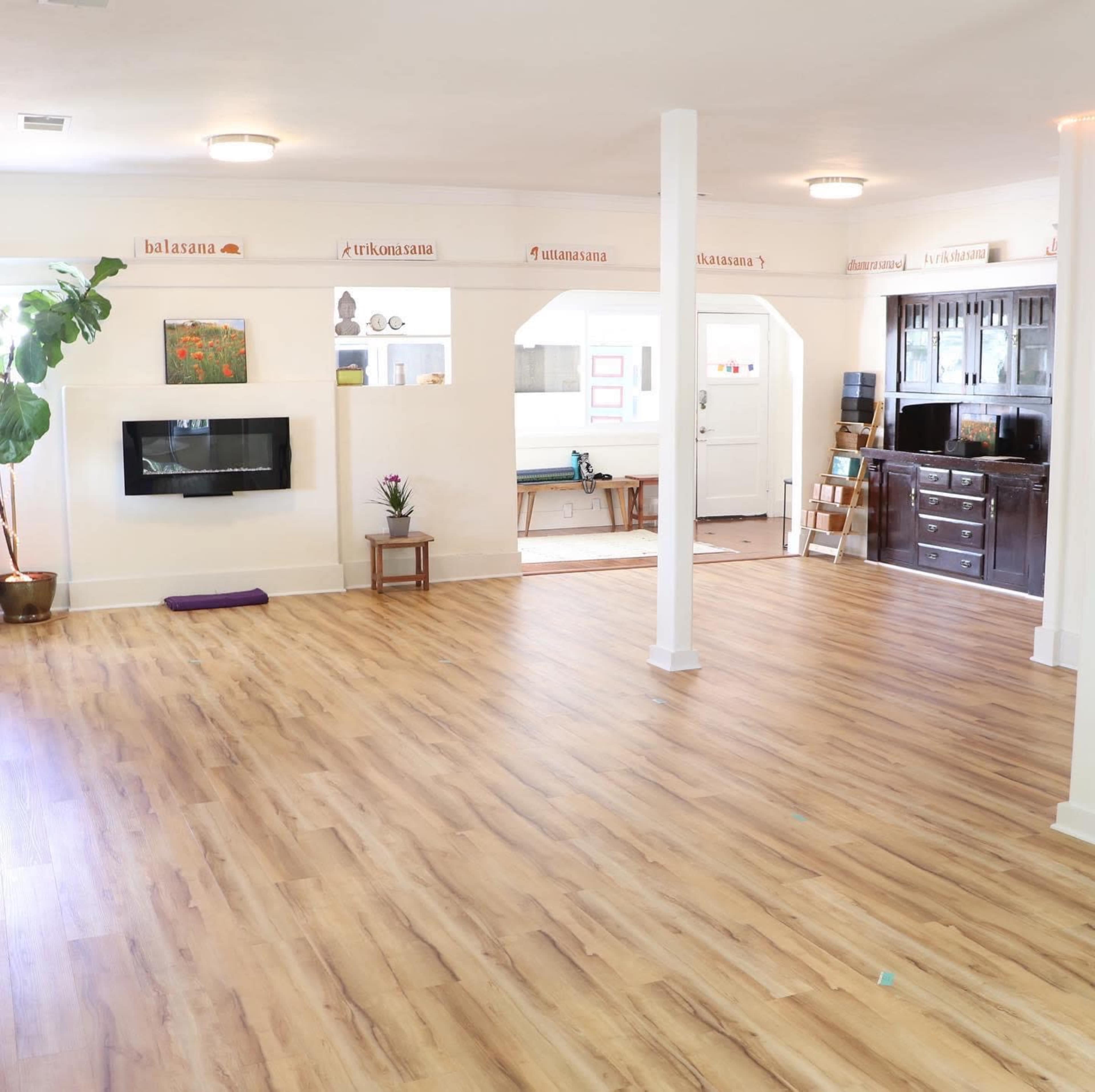 The interior of a spacious, well-lit room features wood flooring, a wall-mounted television, and a cabinet against one wall.