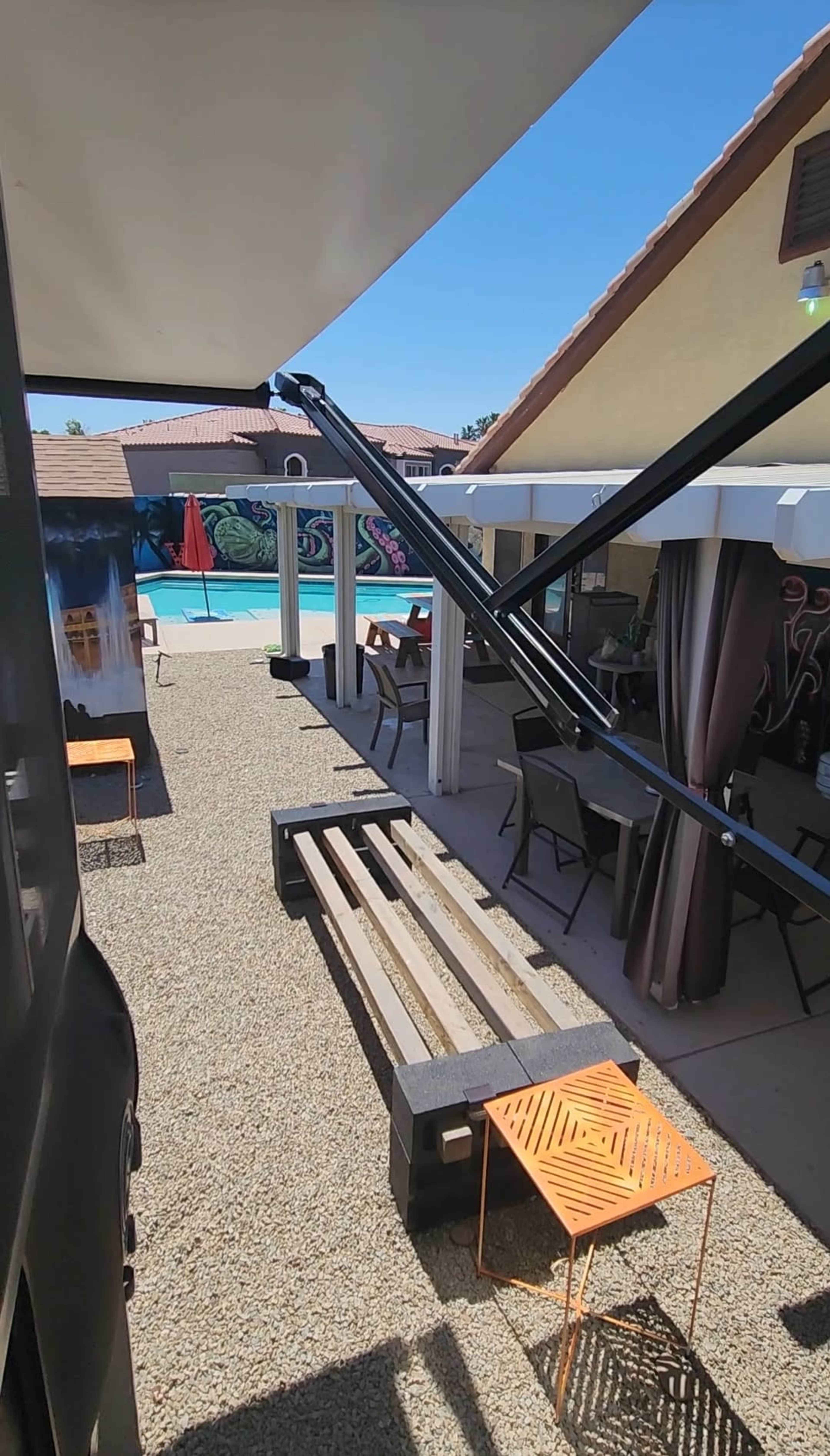 A patio area with tables and chairs overlooking a swimming pool, surrounded by a decorative mural.