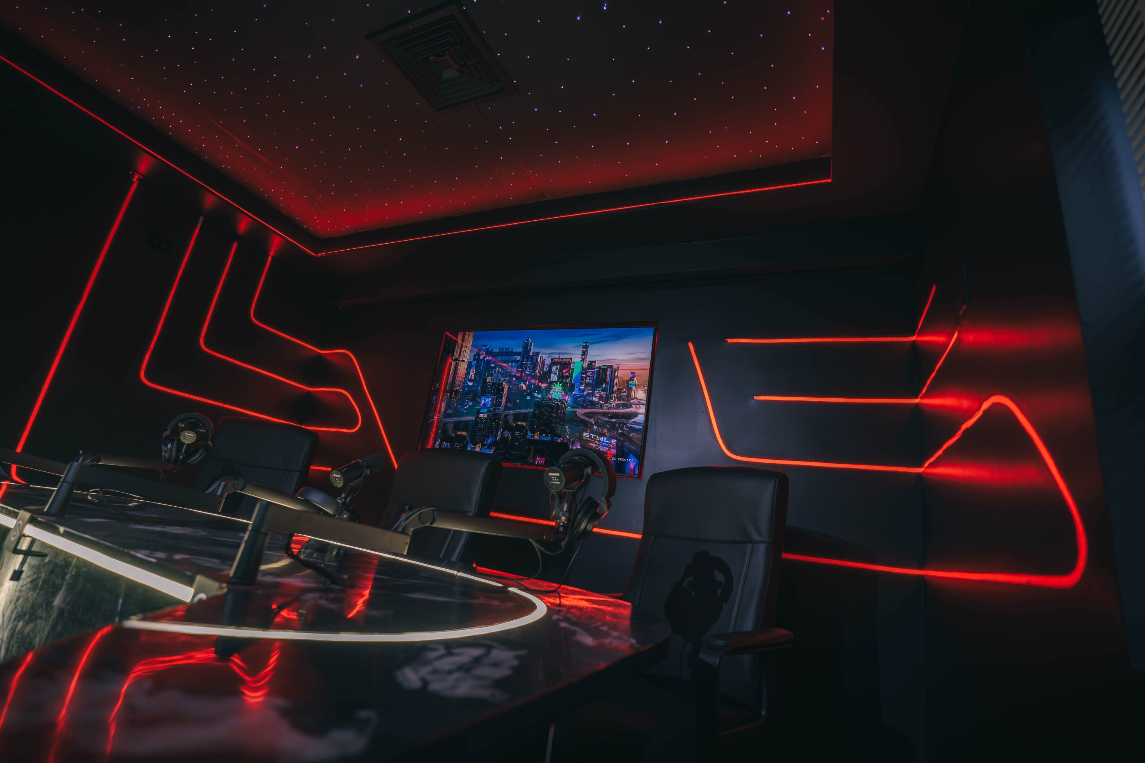 A modern conference room with red neon lighting and a large screen displaying a cityscape.