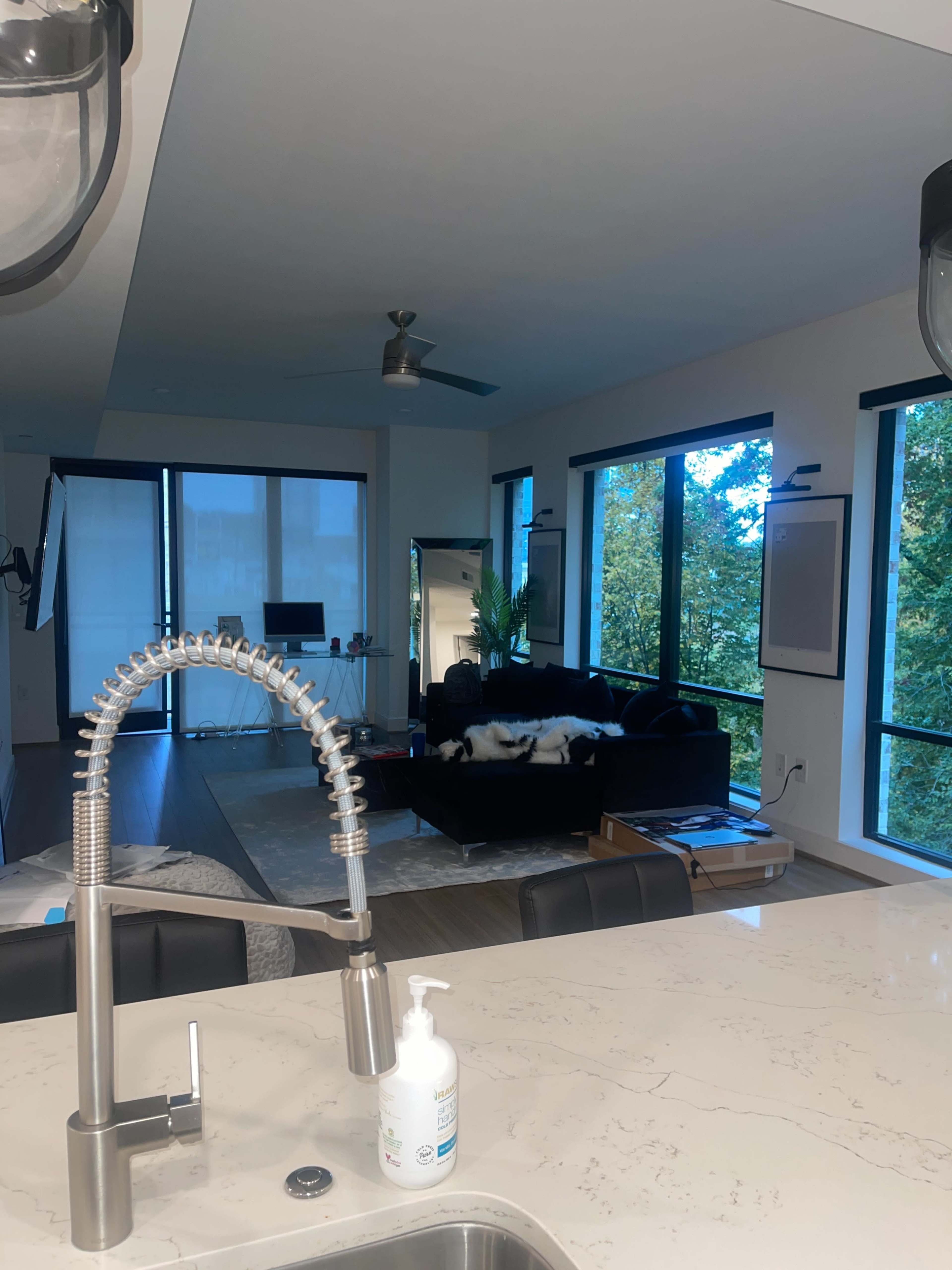 A modern kitchen features a sleek countertop and a view of a living area with large windows and a black couch.