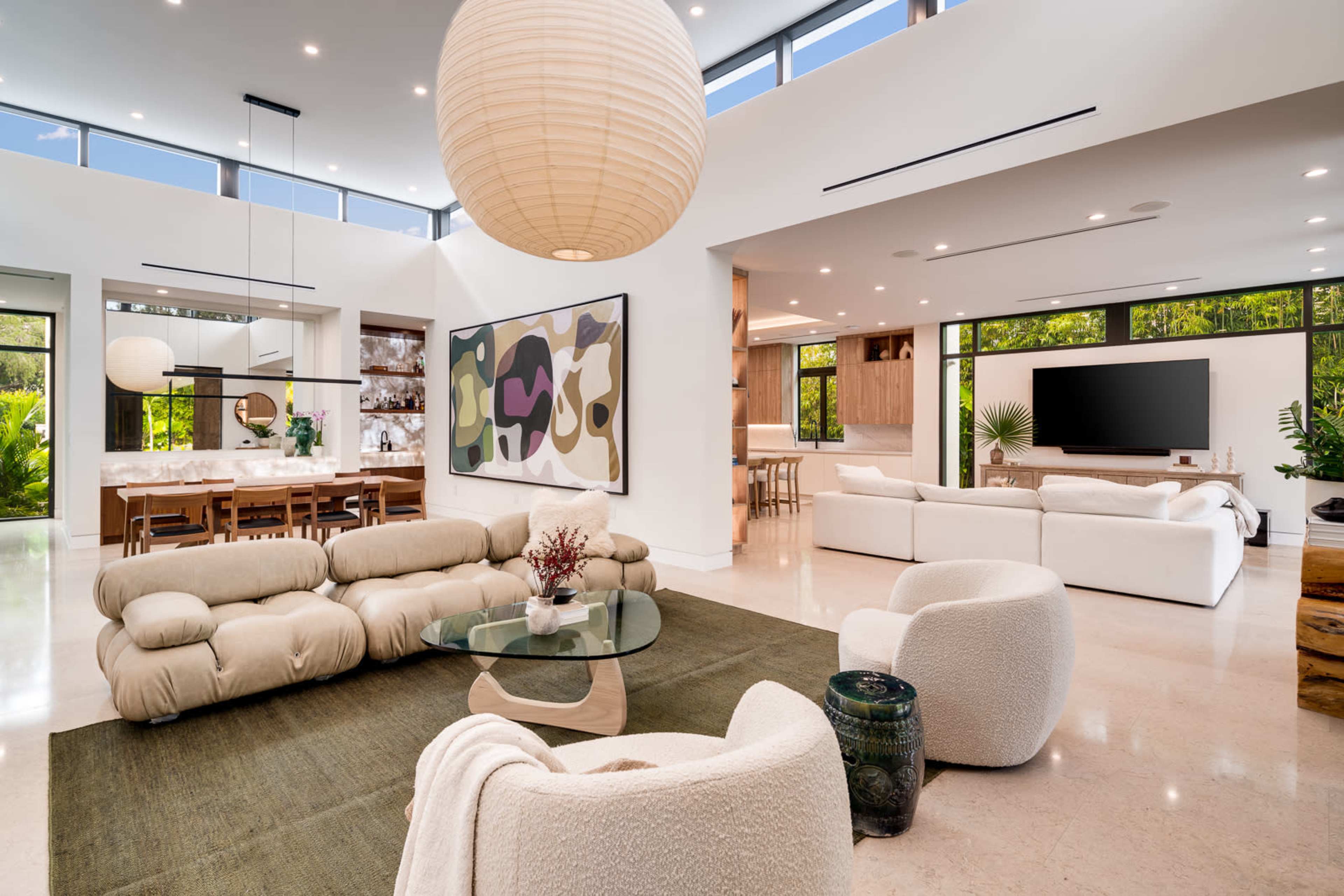 A modern open-concept living space with a large seating area, a dining space, and large windows allowing natural light to fill the room.