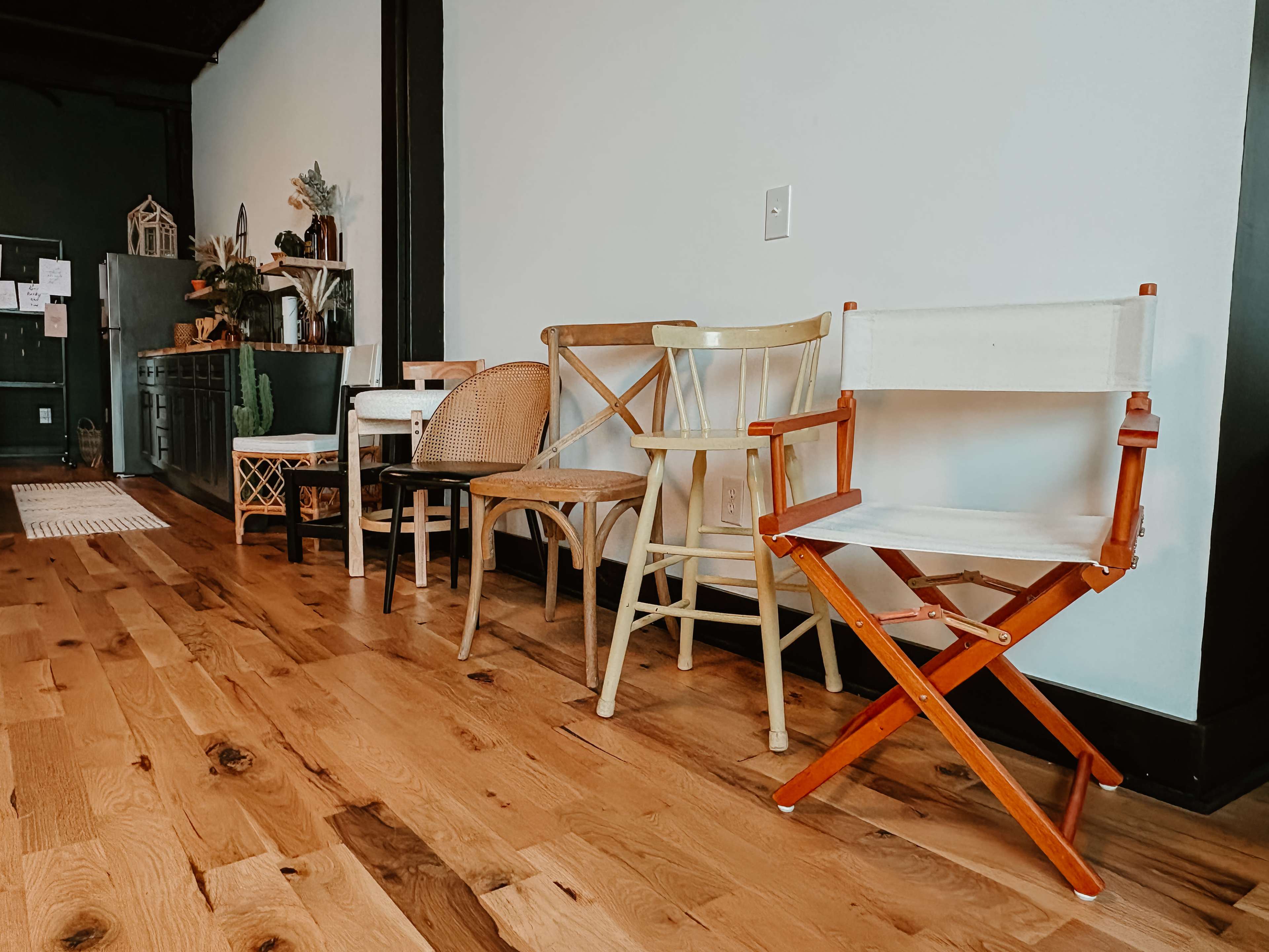 The image shows a row of five different chairs in various styles placed against a wooden floor in a well-lit room.