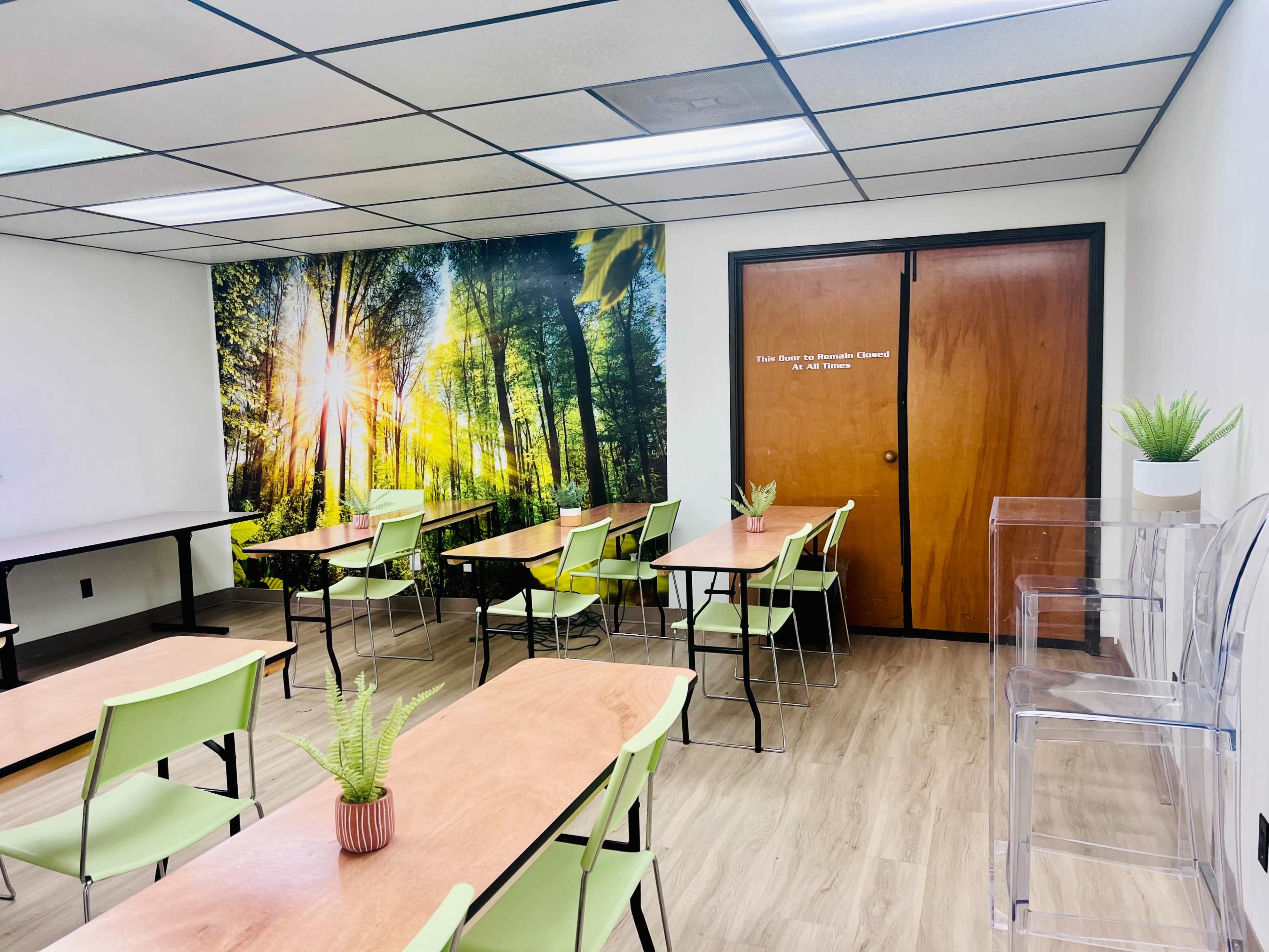 The image shows a classroom with multiple tables and chairs, a large nature-themed mural on one wall, and a closed wooden door labeled "The Room for Research Classes."