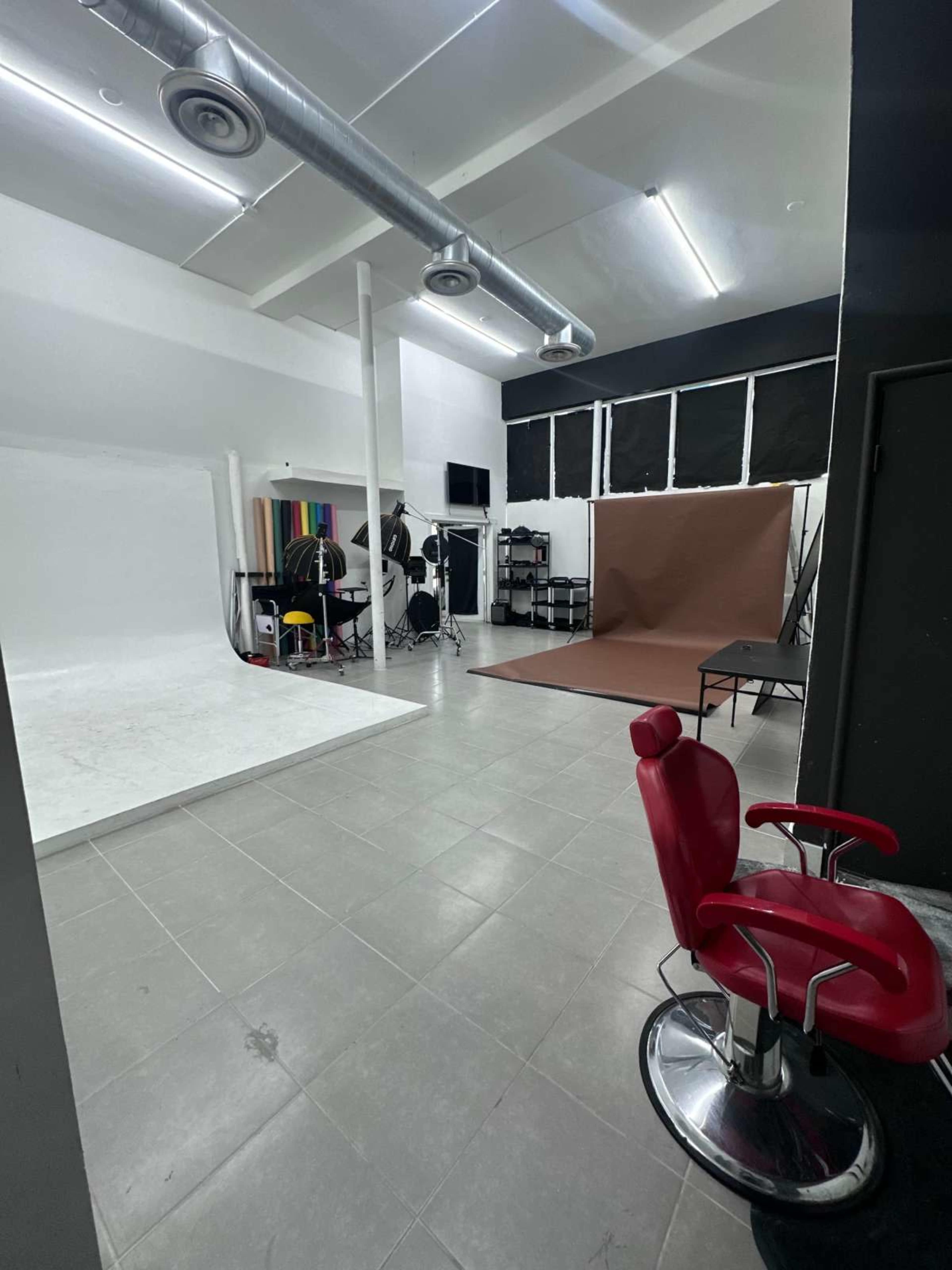 The image shows a spacious studio with a white backdrop, a brown photography backdrop, and a red barber chair.