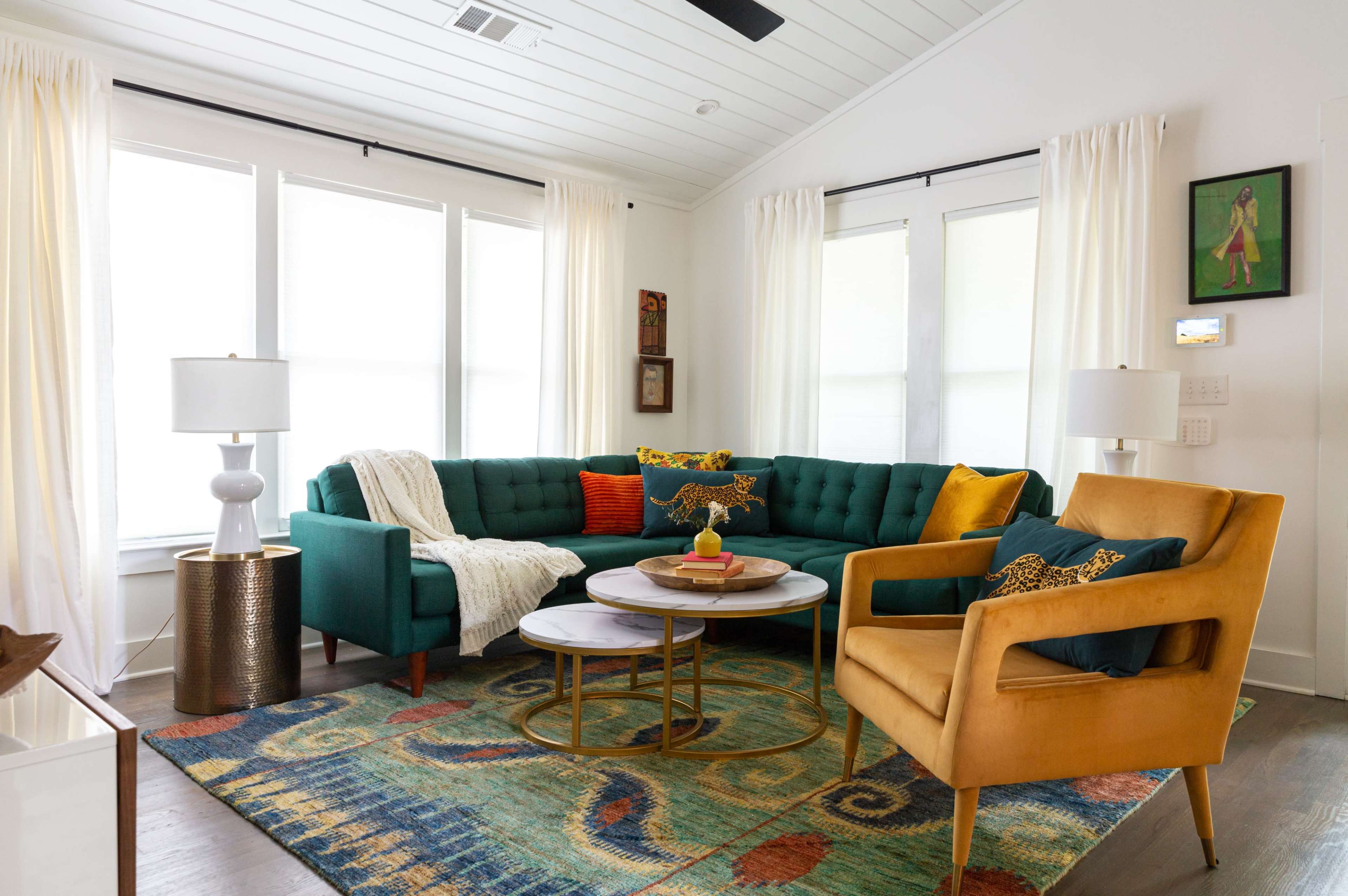 The living room features a green sectional couch, two lamps, a round coffee table, and a colorful area rug under bright windows.