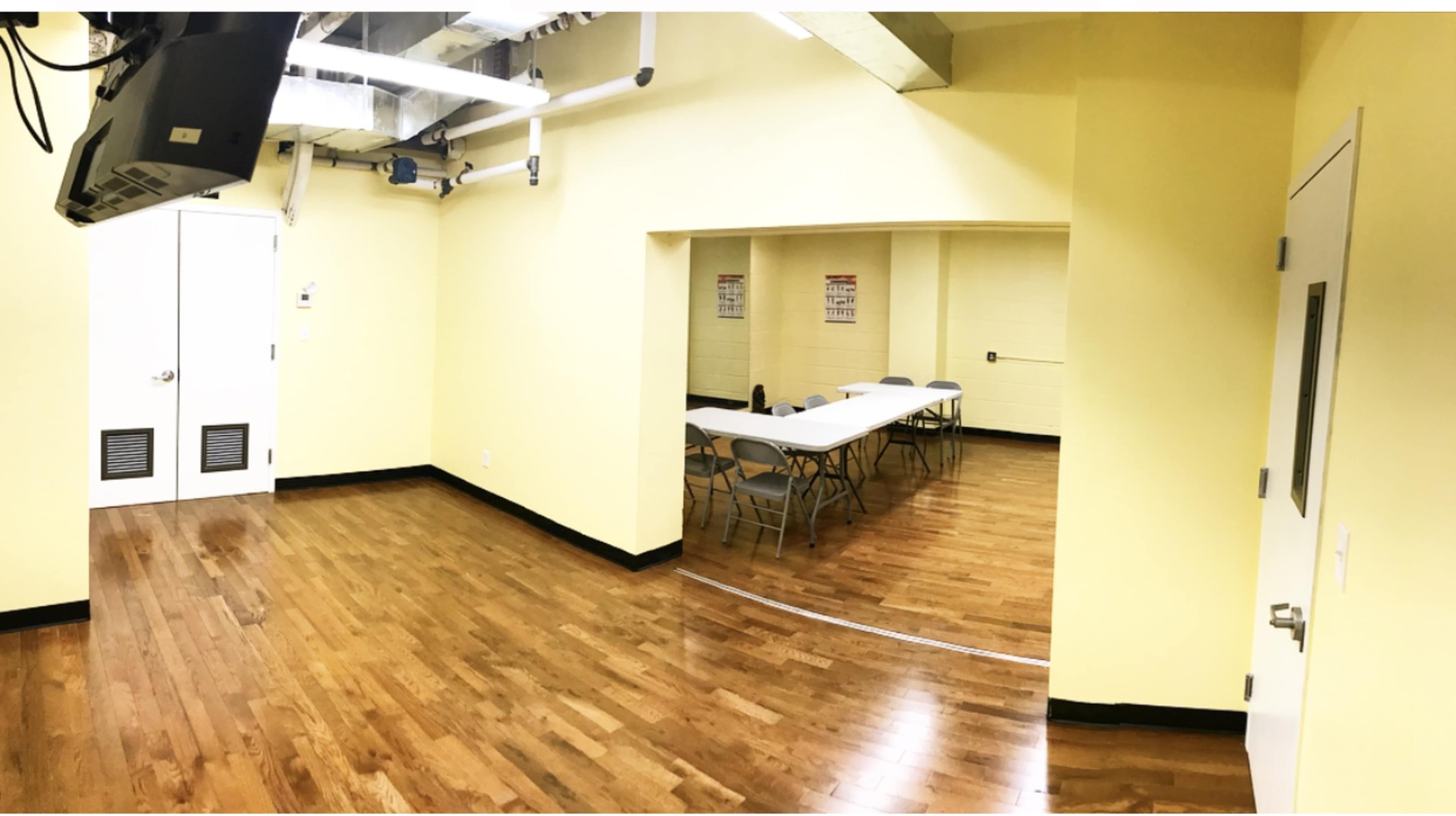 A room with yellow walls, wooden flooring, and a long table with chairs arranged around it, along with a door leading to another room.