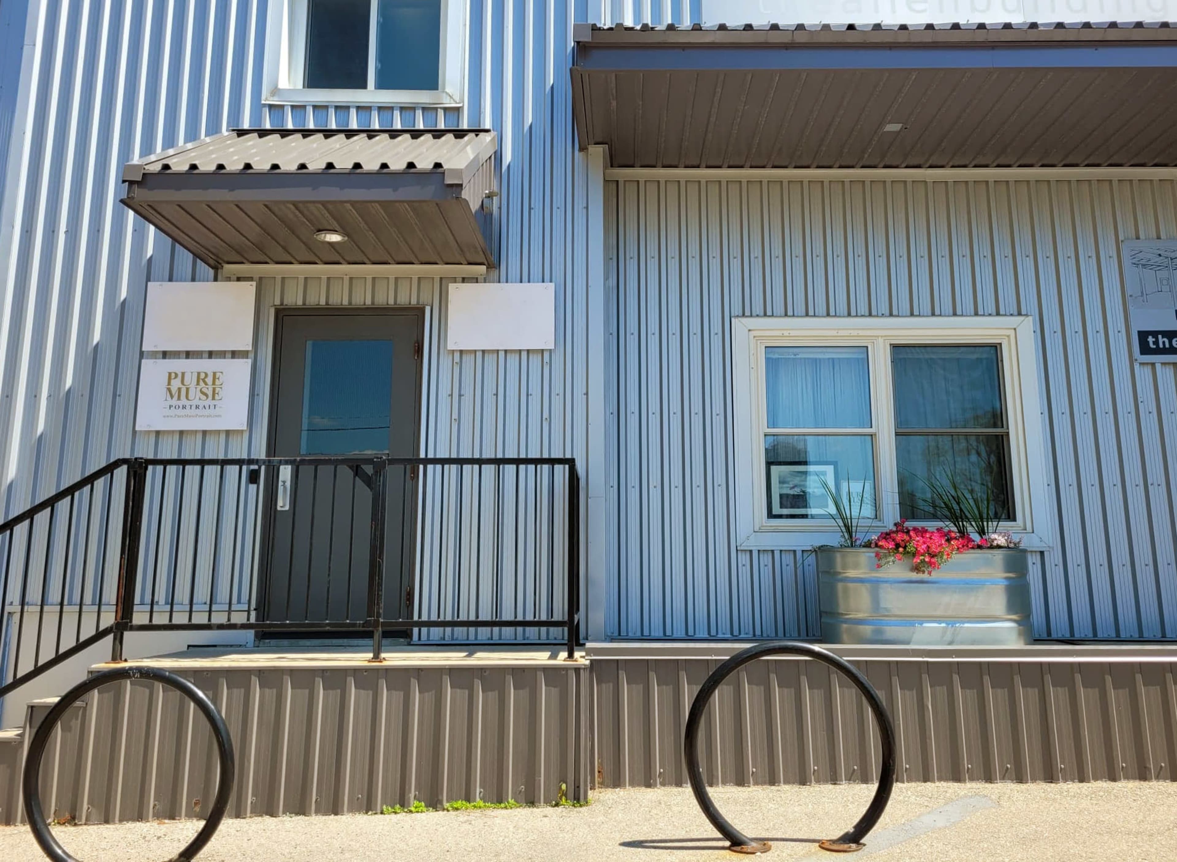 The entrance of a building with a sign for "Pure Muse Restaurant," featuring a metal railing and a decorative planter.