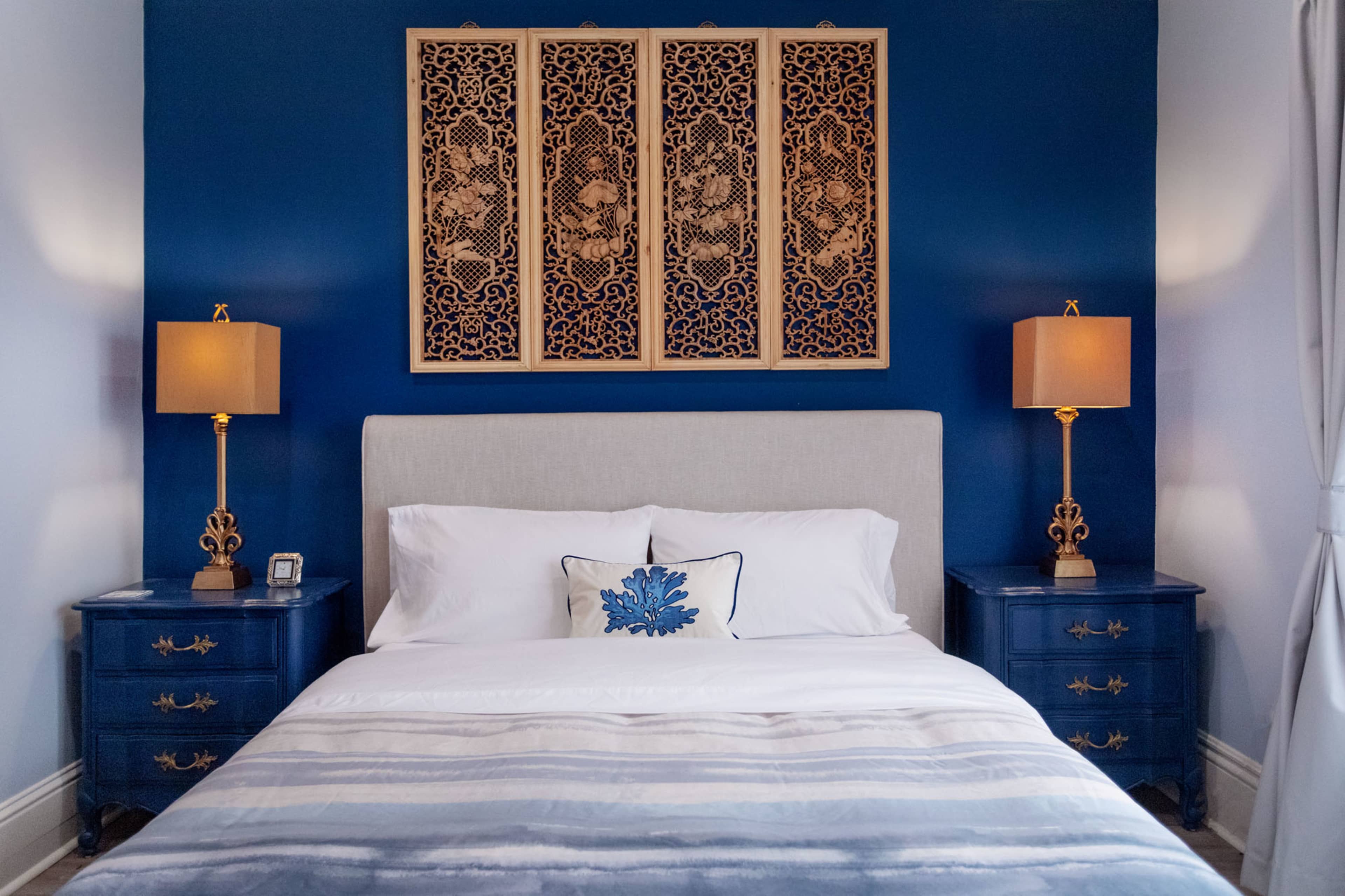A neatly made bedroom with a blue accent wall, a bed with white linens, and two bedside tables with decorative lamps.