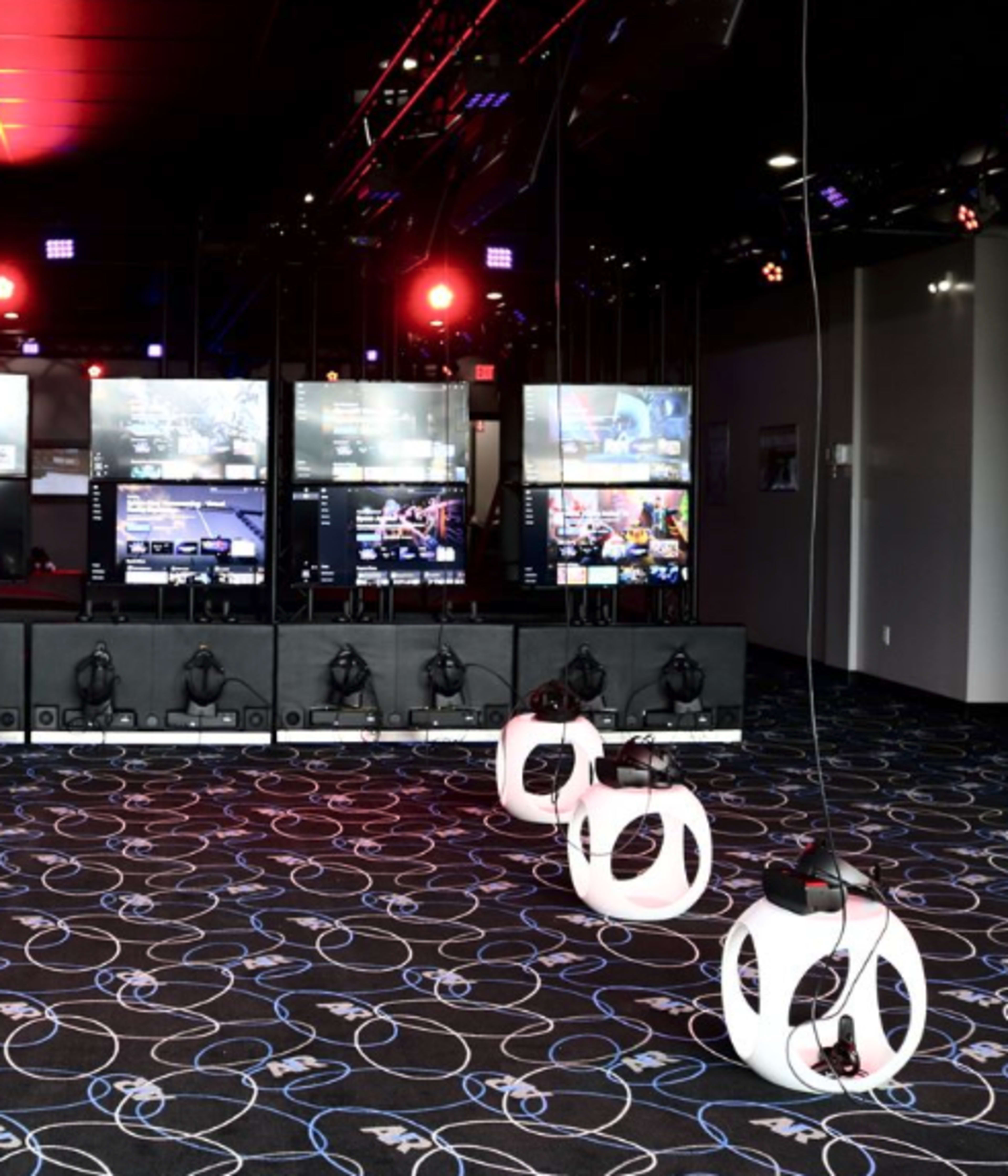 A gaming area with multiple screens displaying gameplay, headset stations, and a patterned carpet.