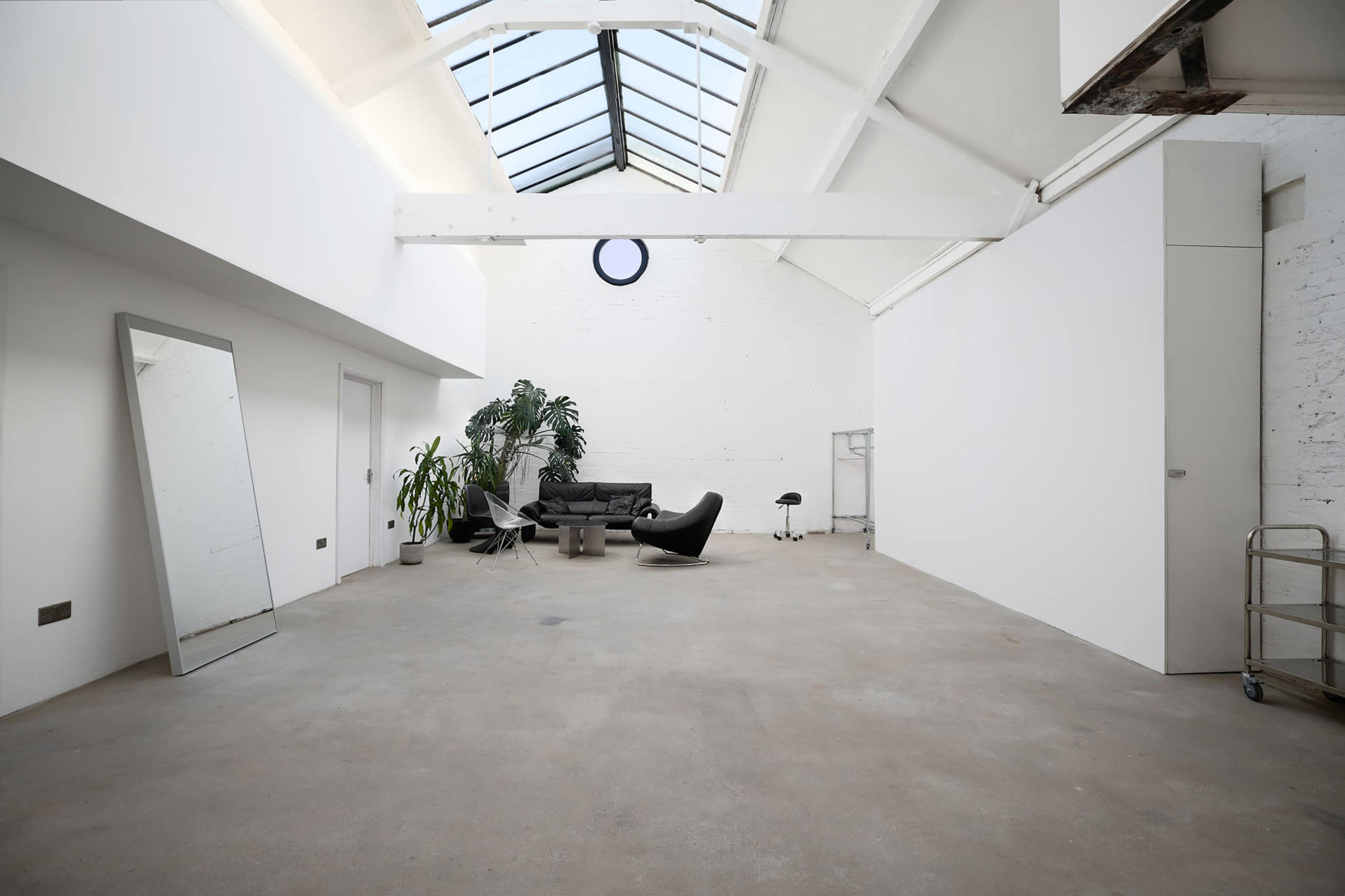 The image shows a spacious, minimalistic interior with large windows, concrete flooring, and modern furniture arranged in a cozy seating area.