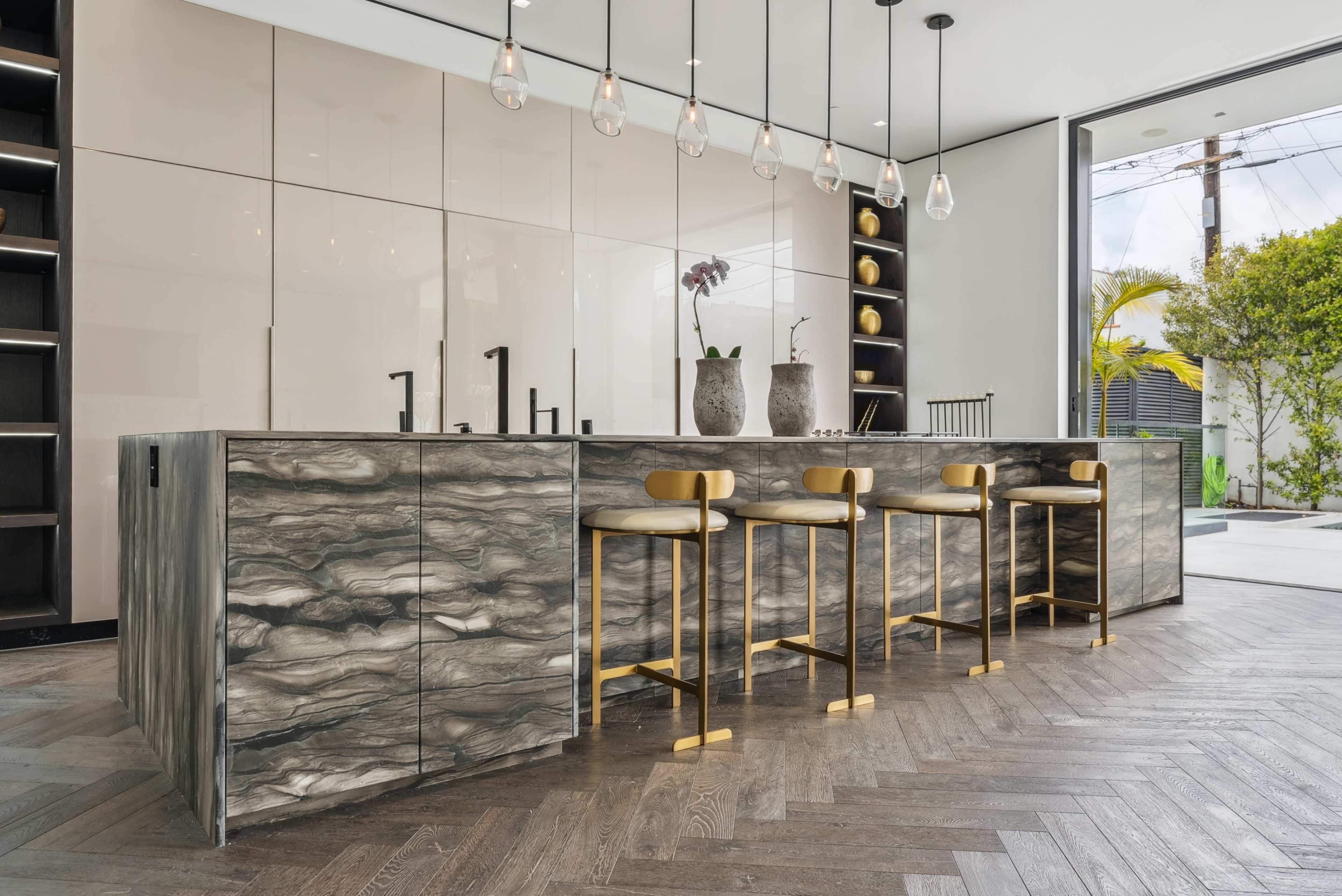 The image shows a modern kitchen featuring a large, textured island with four gold-accented stools and pendant lighting above.